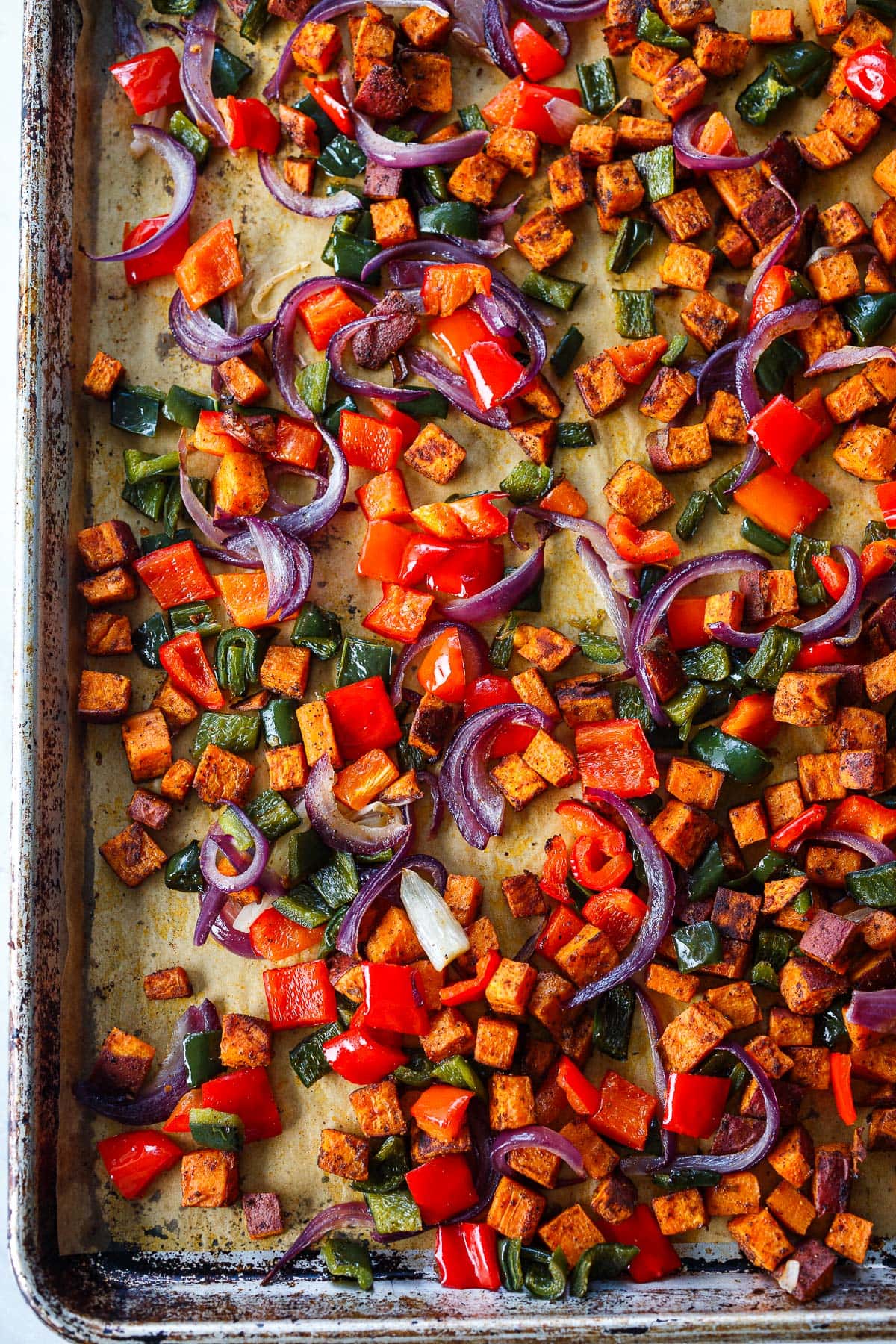 parchment-lined baking sheet with sweet potato hash with peppers and onions.