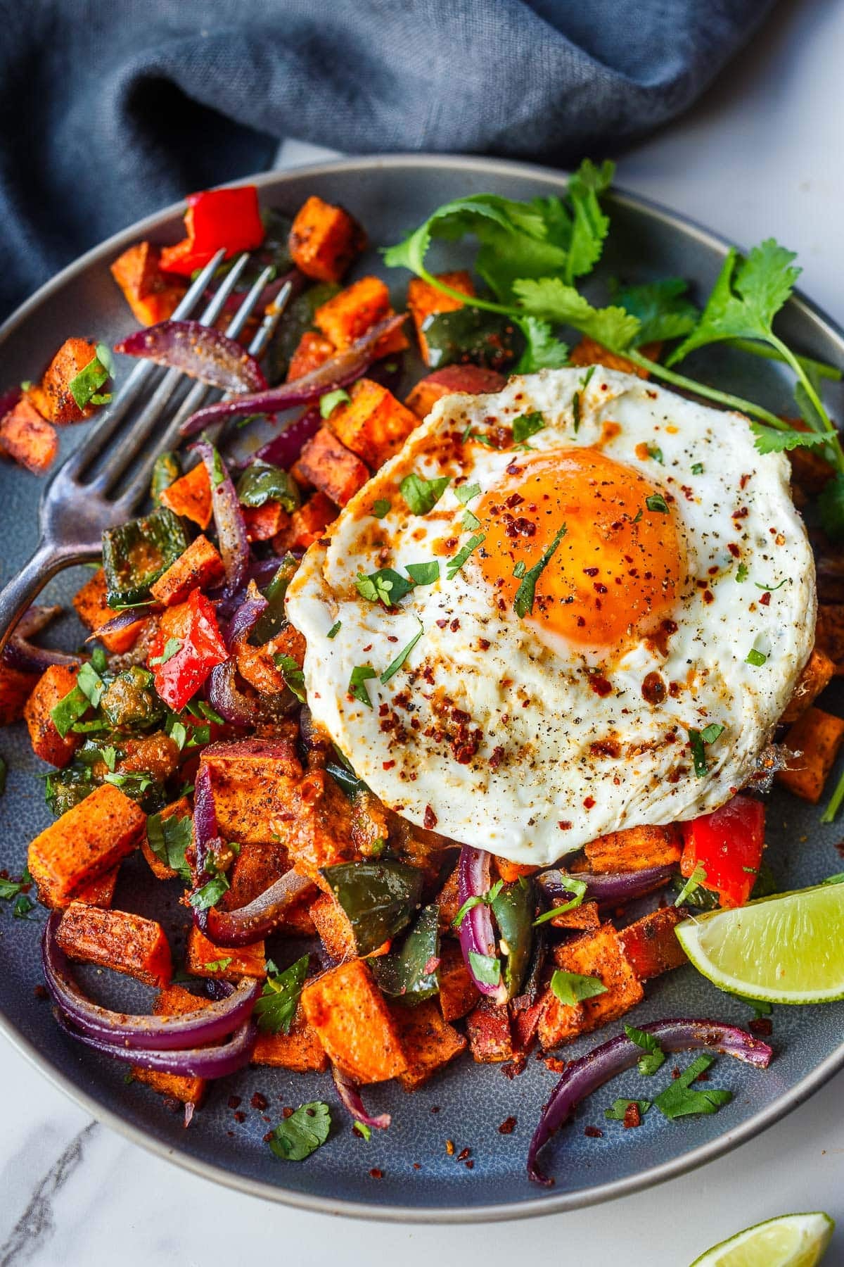 plate of sweet potato hash topped with a fried egg, chili flakes, and herbs. 