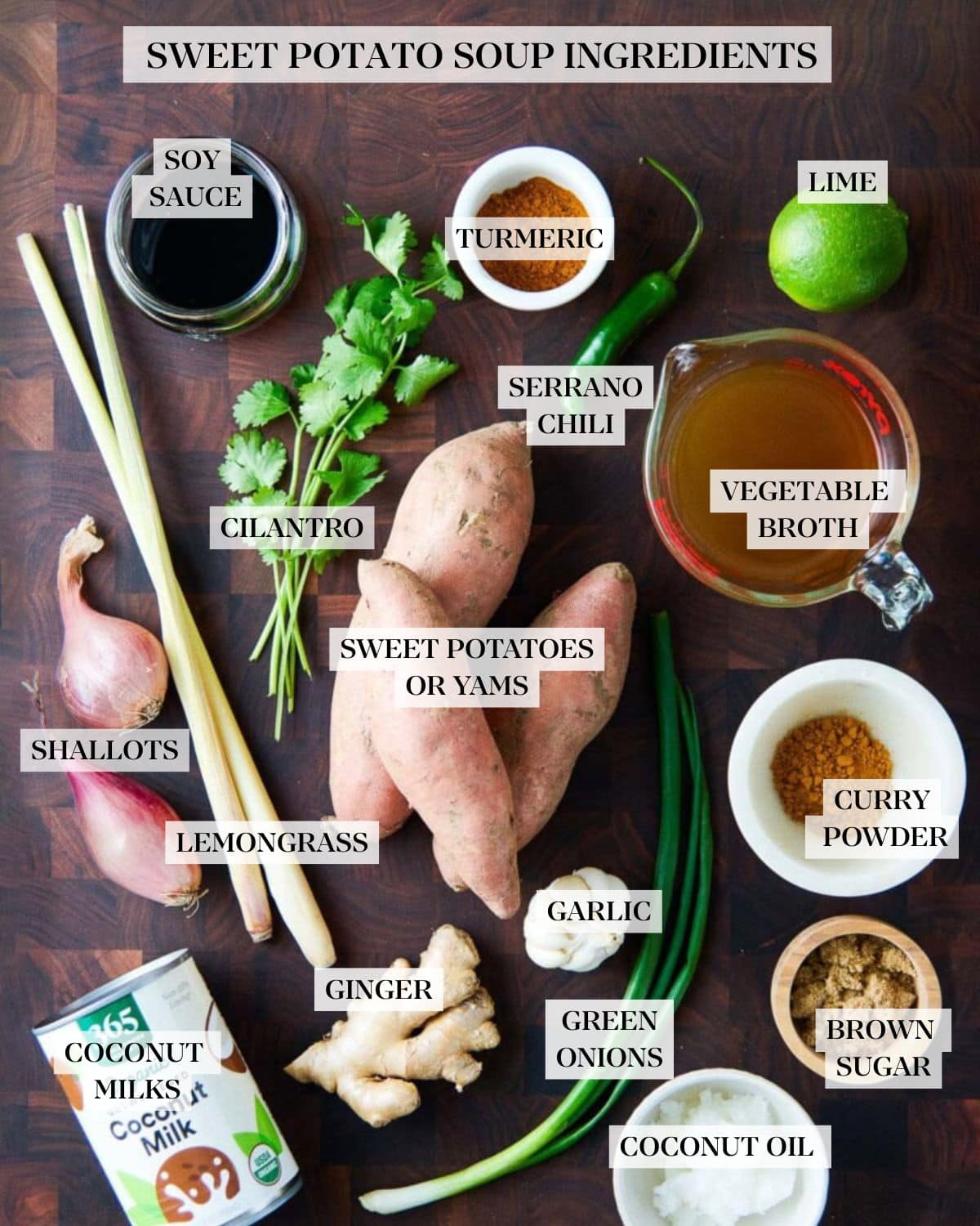 ingredients for sweet potato soup laid out on wood butcher block - soy sauce, cilantro, curry powder, serrano chili, lime, broth, sweet potatoes, turmeric, lemongrass, shallot, garlic, ginger, brown sugar, coconut milk, coconut oil, scallions.