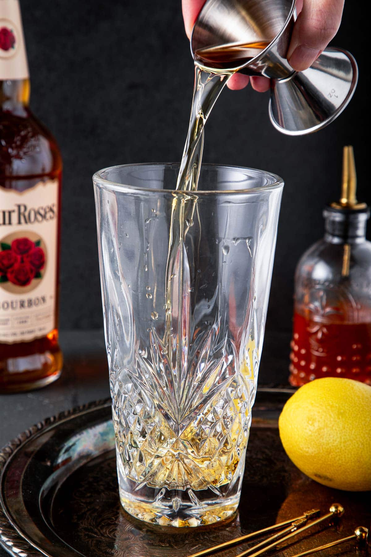 hand pouring bourbon whiskey from jigger into glass shaker. 