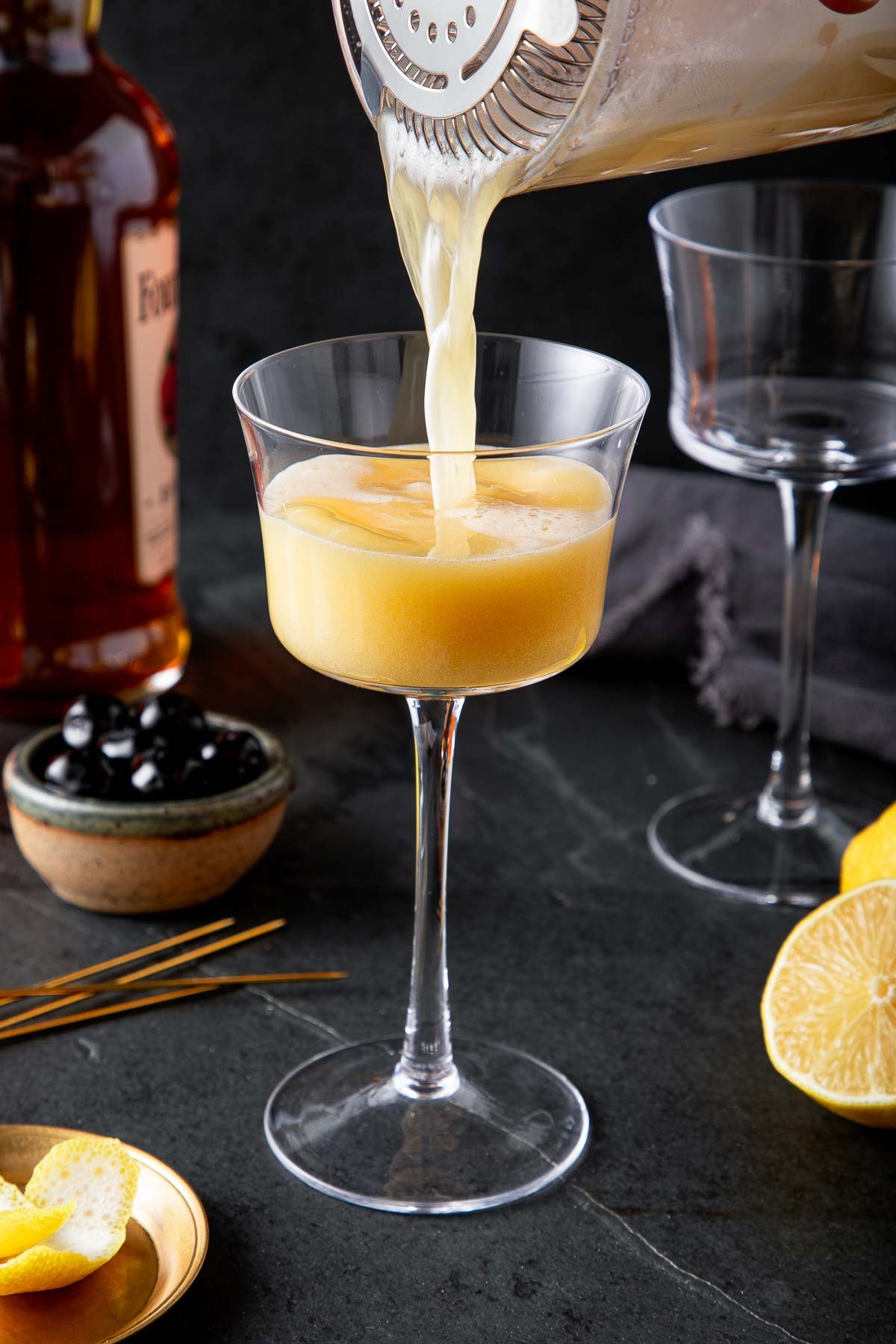 pouring classic whiskey sour from shaker into coupe glass. 