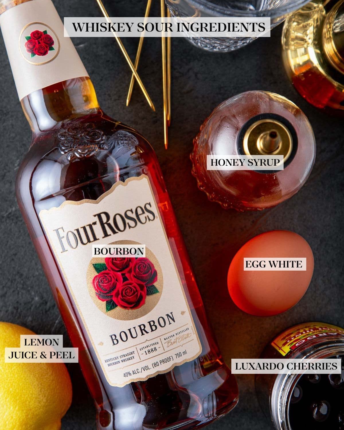 ingredients for classic whiskey sour - glass shaker, brass toothpicks, honey simple syrup, egg, FourRoses bourbon, lemon, Luxardo cherries.