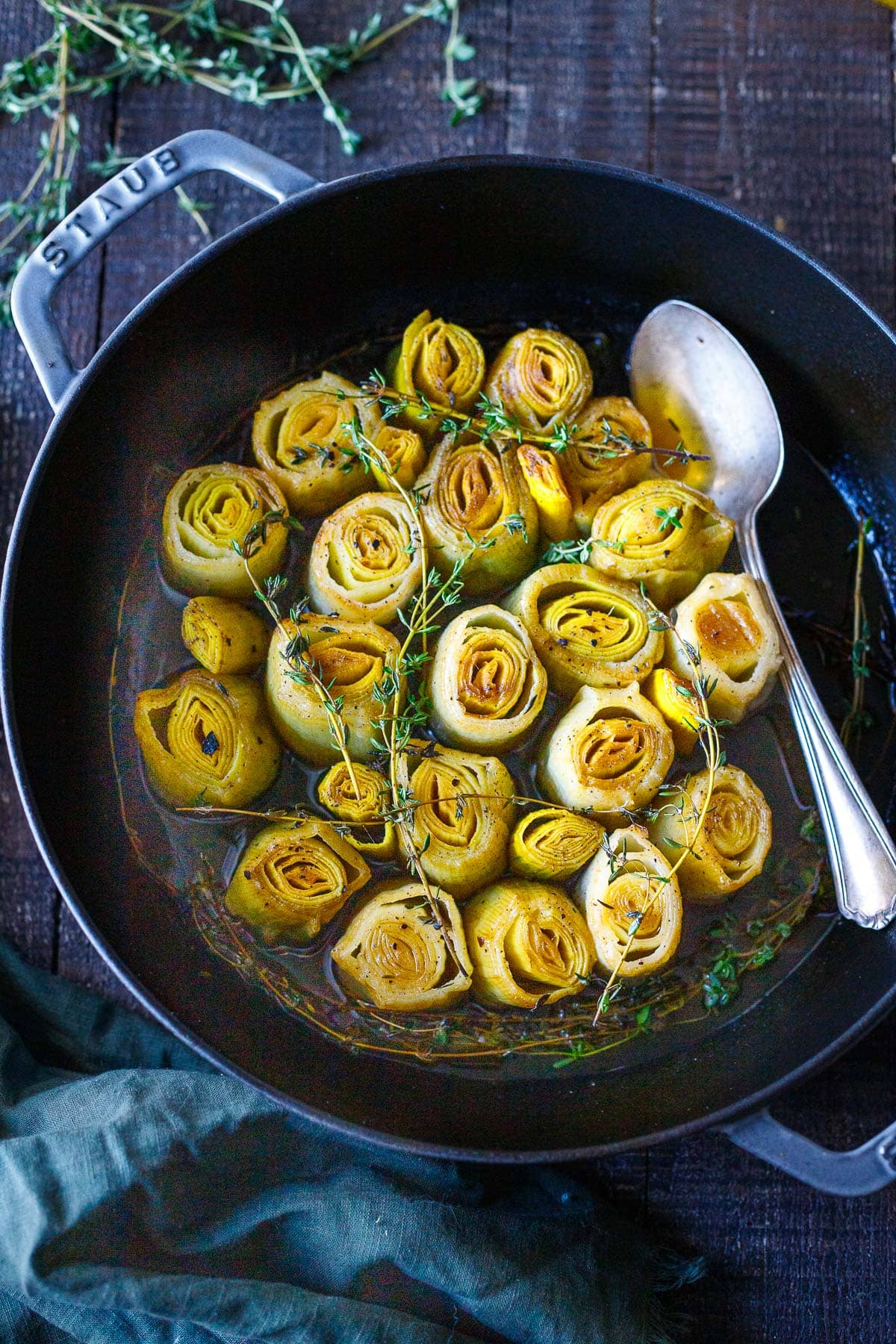 dutch oven with braised leeks topped with thyme sprigs with spoon in dish. 