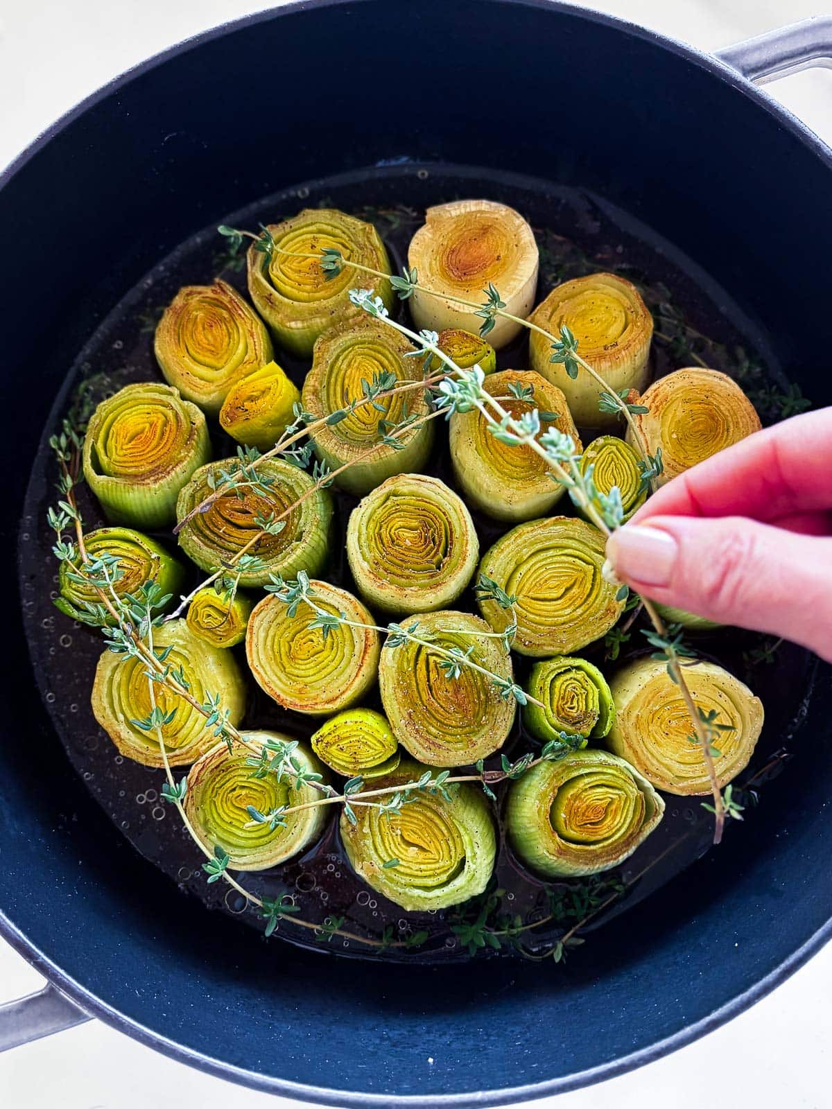 hand placing thyme sprigs on top of seared leeks. 