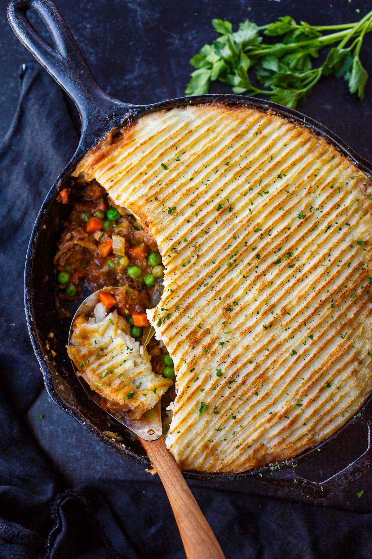 cottage pie in cast iron skillet with mashed potato topping with spoon scooping some of the veggie meat filling.