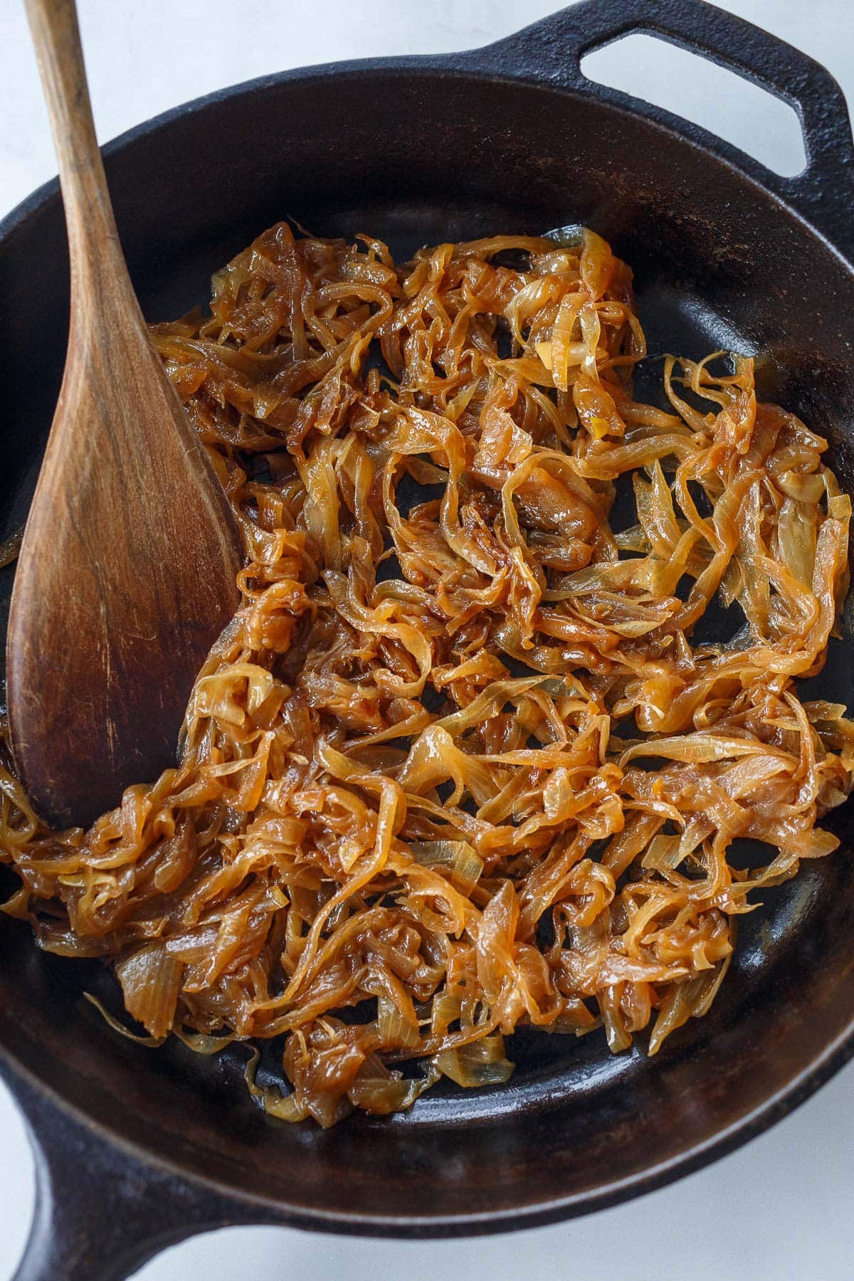 wood spoon stirring caramelized onions in cast iron skillet. 