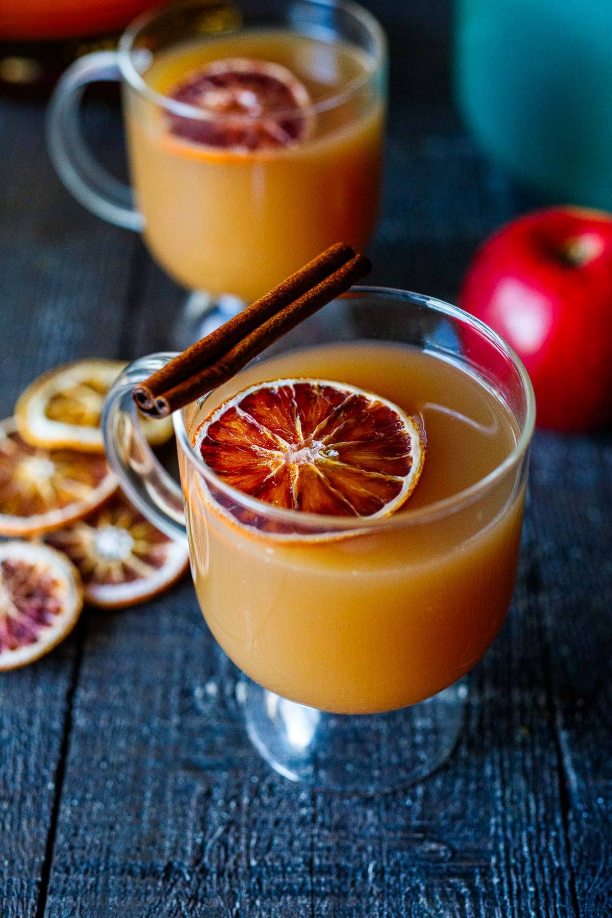 hot bourbon apple cider in a glass mug with dried orange slice with cinnamon stick on the rim.