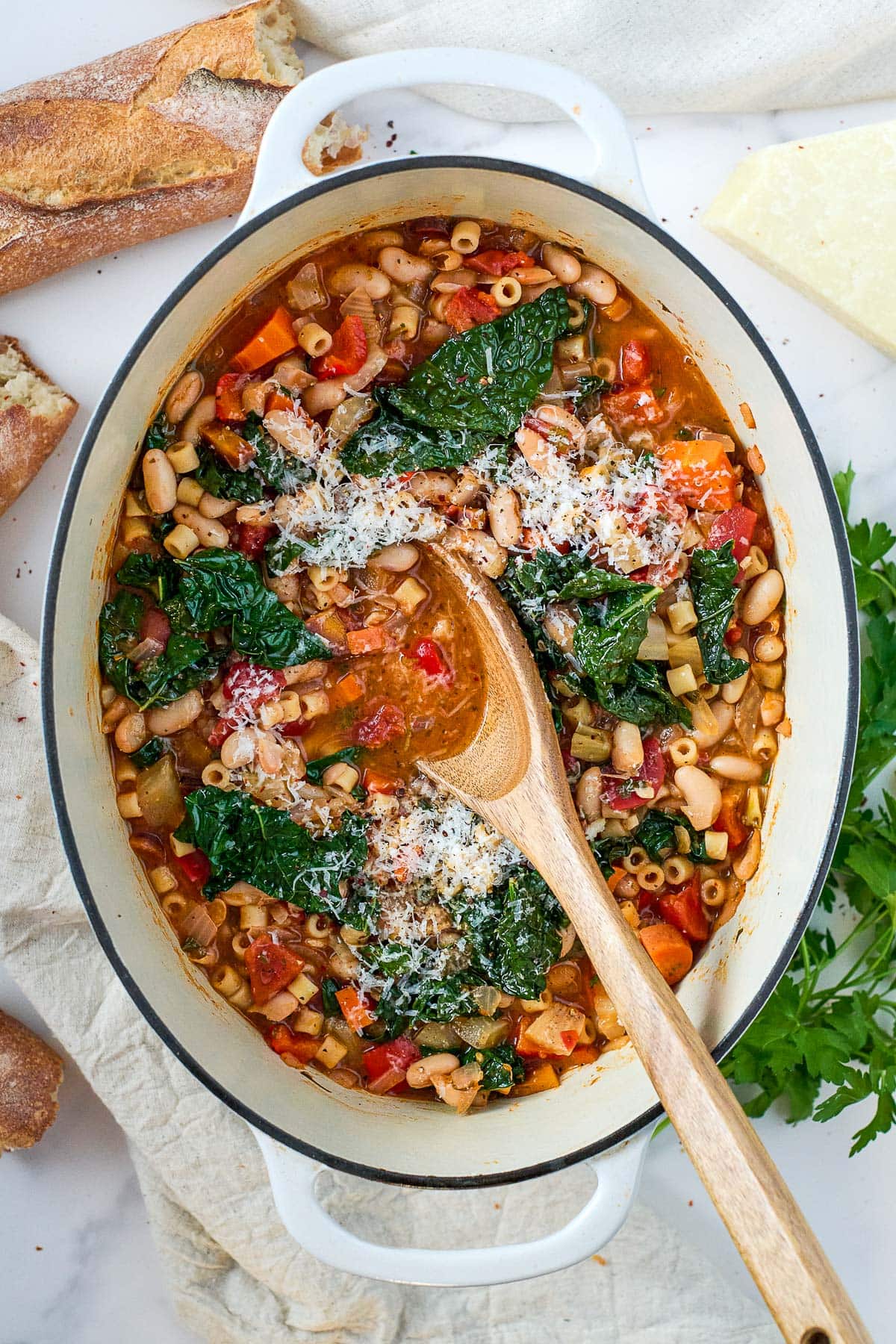 oval dutch oven with minestrone soup with kale and grated pecorino cheese with wood serving spoon.