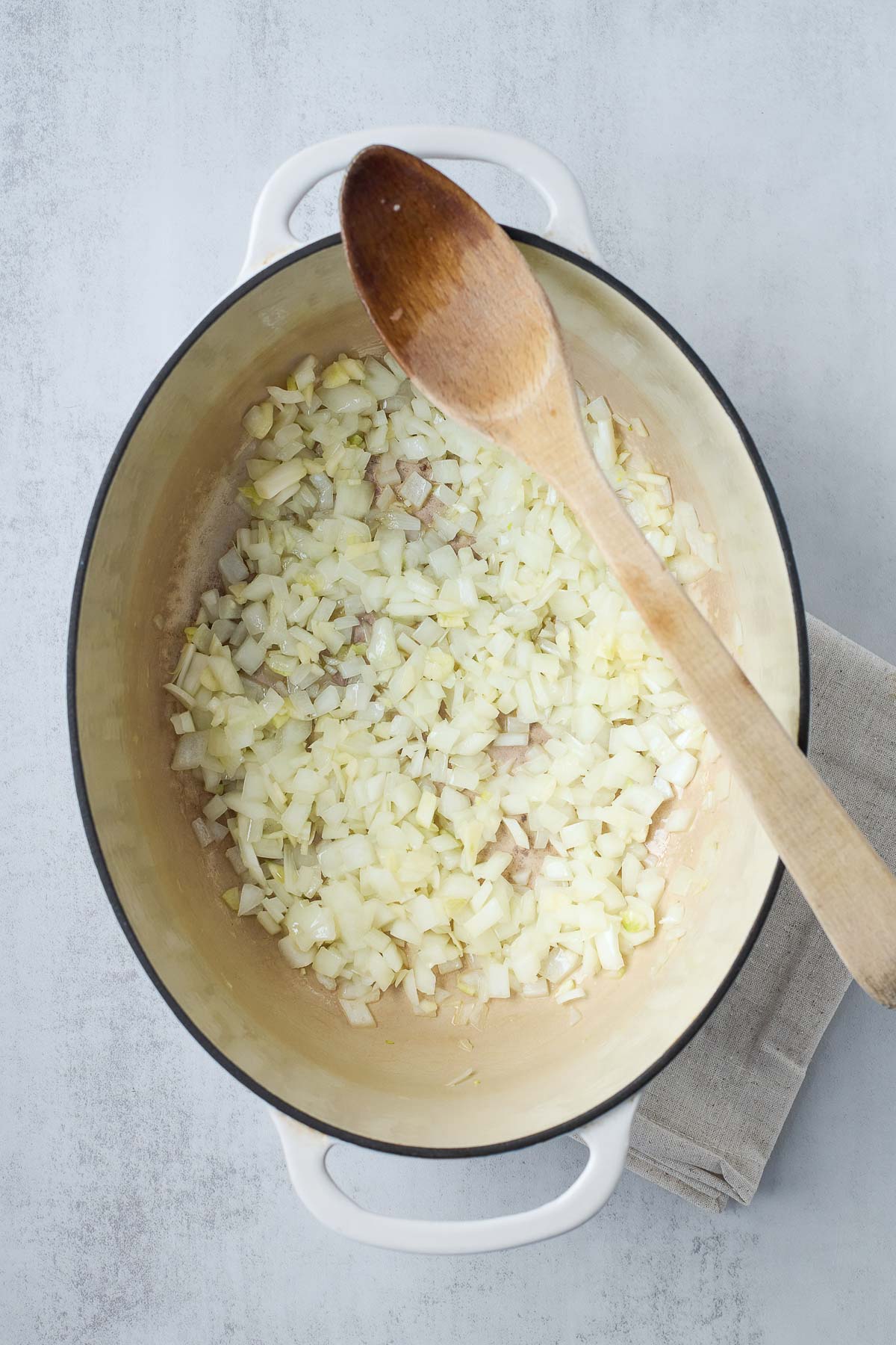 diced onions sautéing in dutch oven with wooden spoon resting on top.