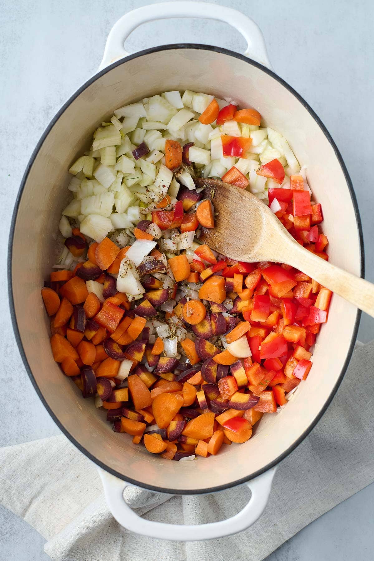 dutch oven with diced vegetables. -onion, red bell pepper, and carrots, with spices and wooden spoon.