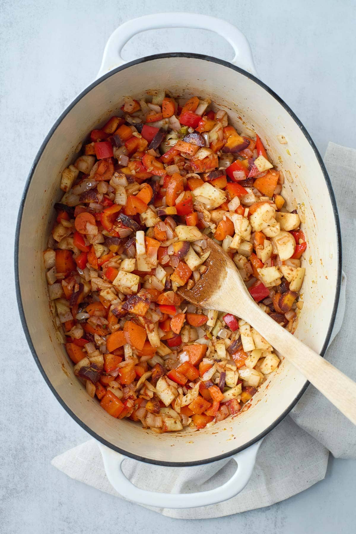 dutch oven with vegetables sautéing with wooden spoon to prep minestrone soup.