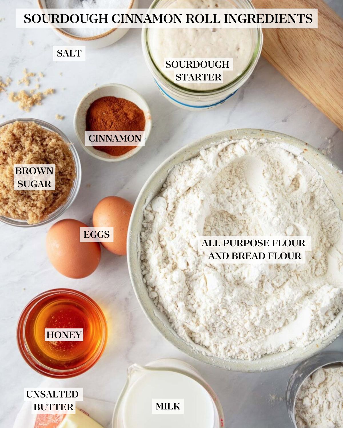 ingredients for sourdough cinnamon rolls - salt, sourdough starter, cinnamon, brown sugar, eggs, flour, honey, butter, milk, bread flour, next to rolling pin.