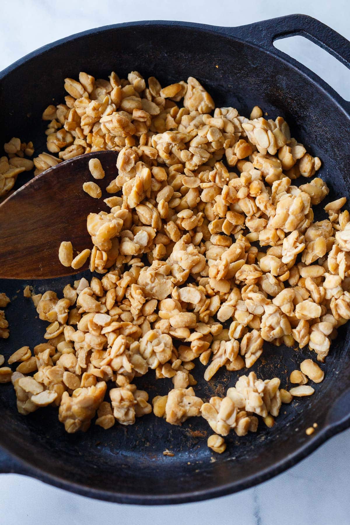 crumbled tempeh in cast iron skillet with wooden spoon. 
