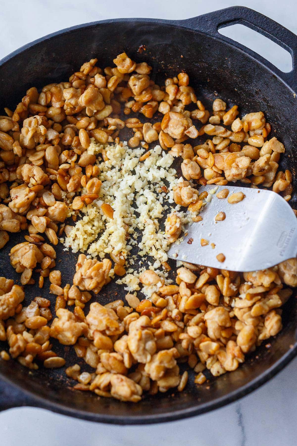 sautéed tempeh in cast iron skillet with minced garlic and ginger with metal spatula to stir. 
