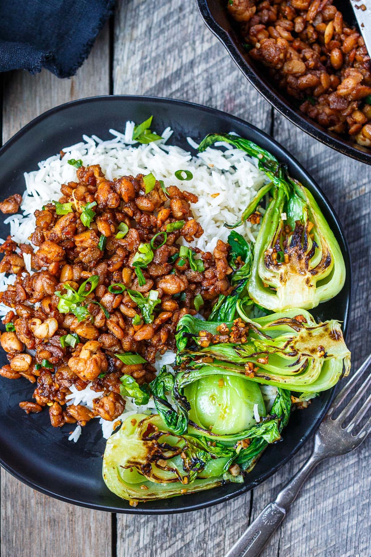 A plate of sticky stir-fried tempeh on rice with stir-fried bok choy.