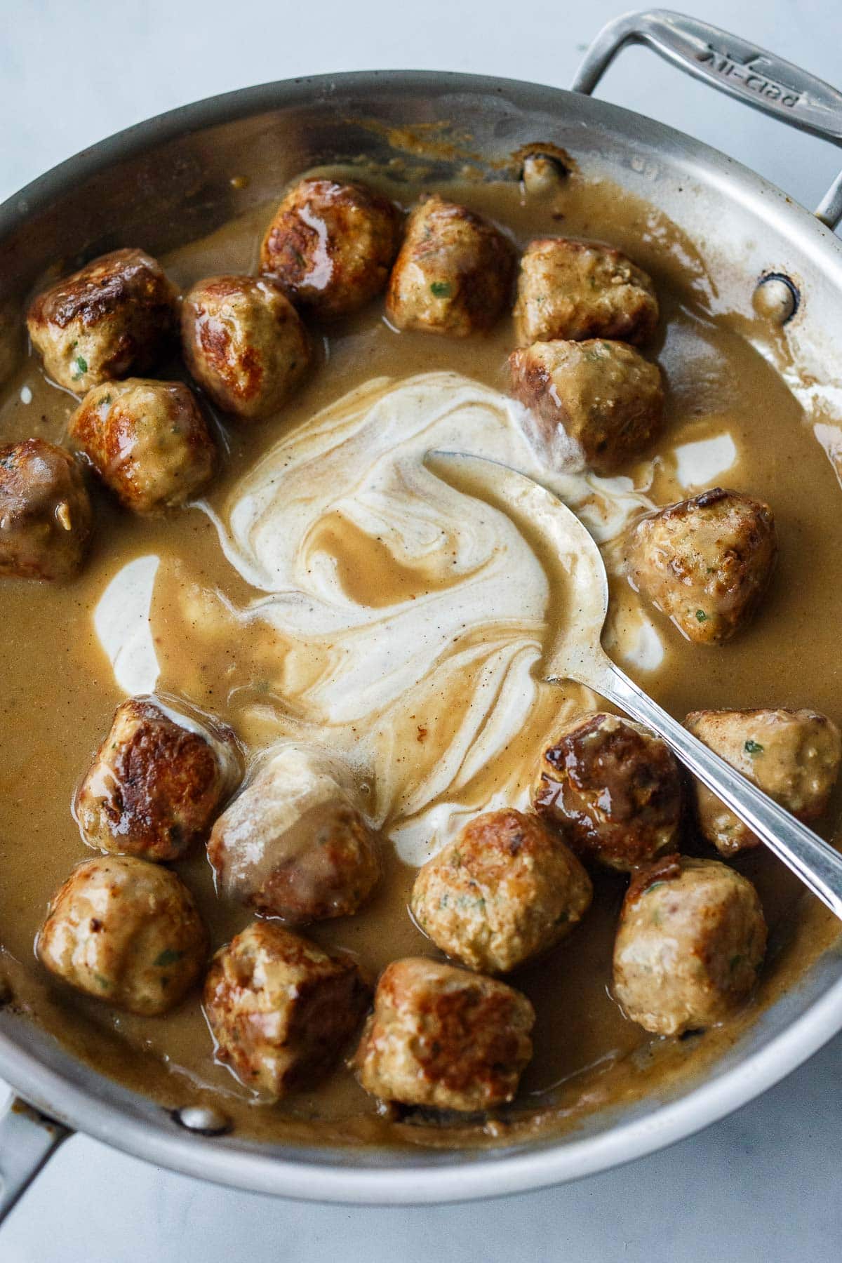 spoon mixing heavy cream into pan with Swedish meatballs and gravy.