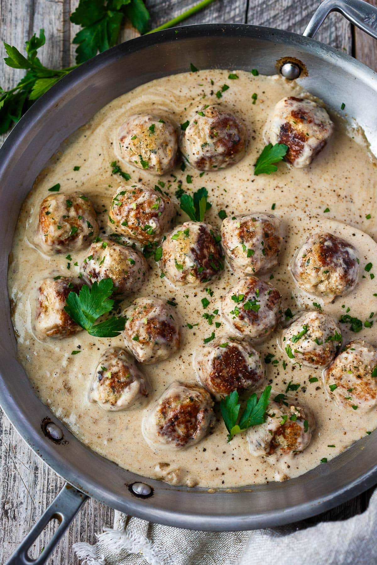 frying pan with Swedish meatballs in brown gravy, garnished with fresh parsley.