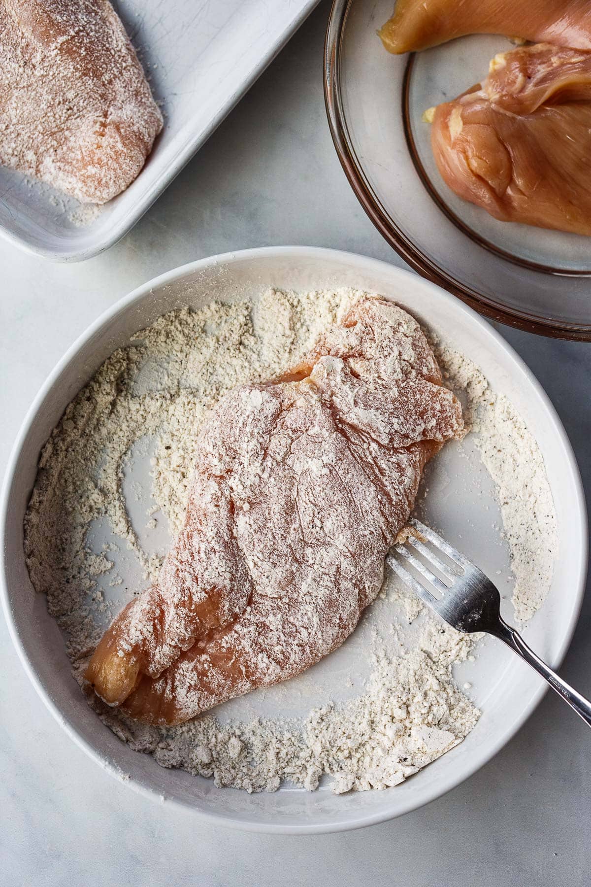 chicken breast dredged in flour on plate with fork. 