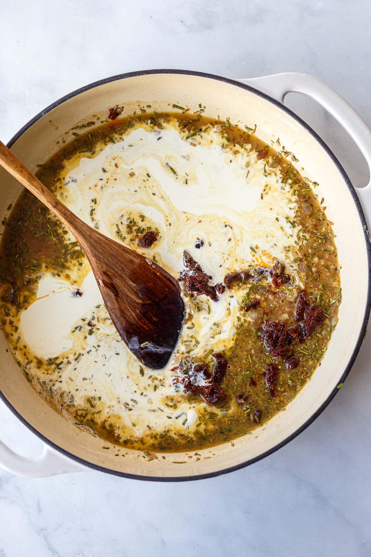 dutch oven with creamy Tuscan sauce with wood spoon, stirring heavy cream and sun-dried tomatoes in. 