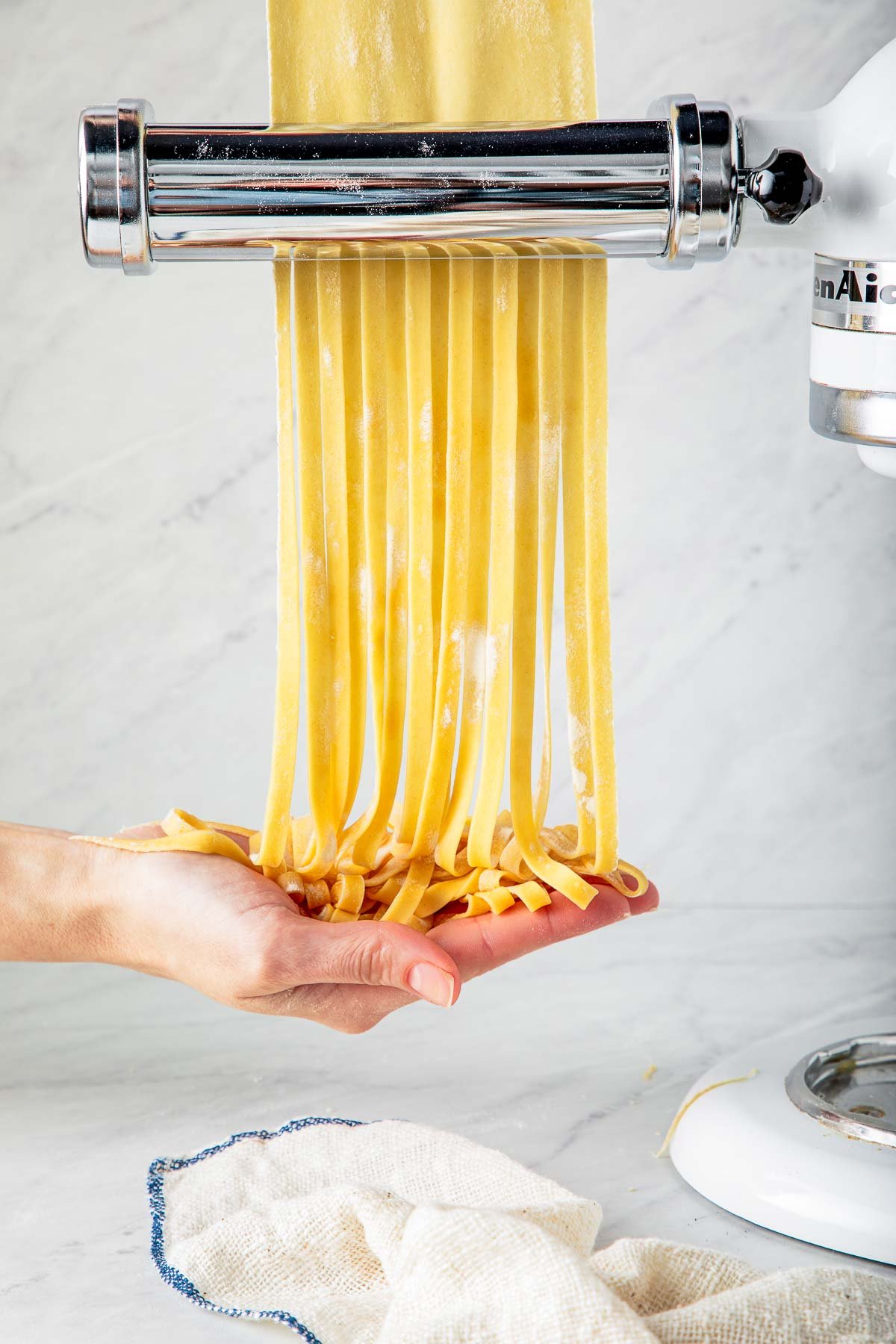 thin homemade pasta dough going through pasta cutter to create long strands that fall into the palm of a hand.