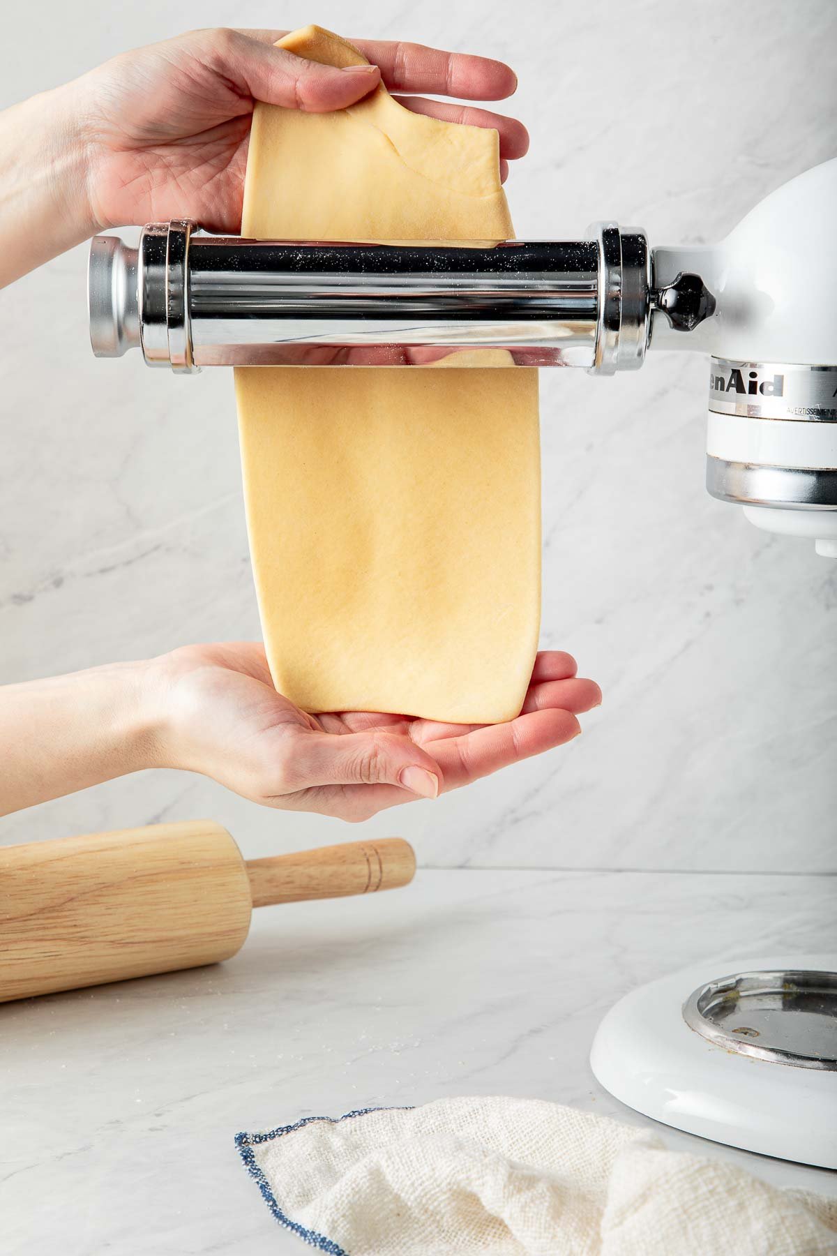 hands rolling homemade pasta dough through pasta maker. 
