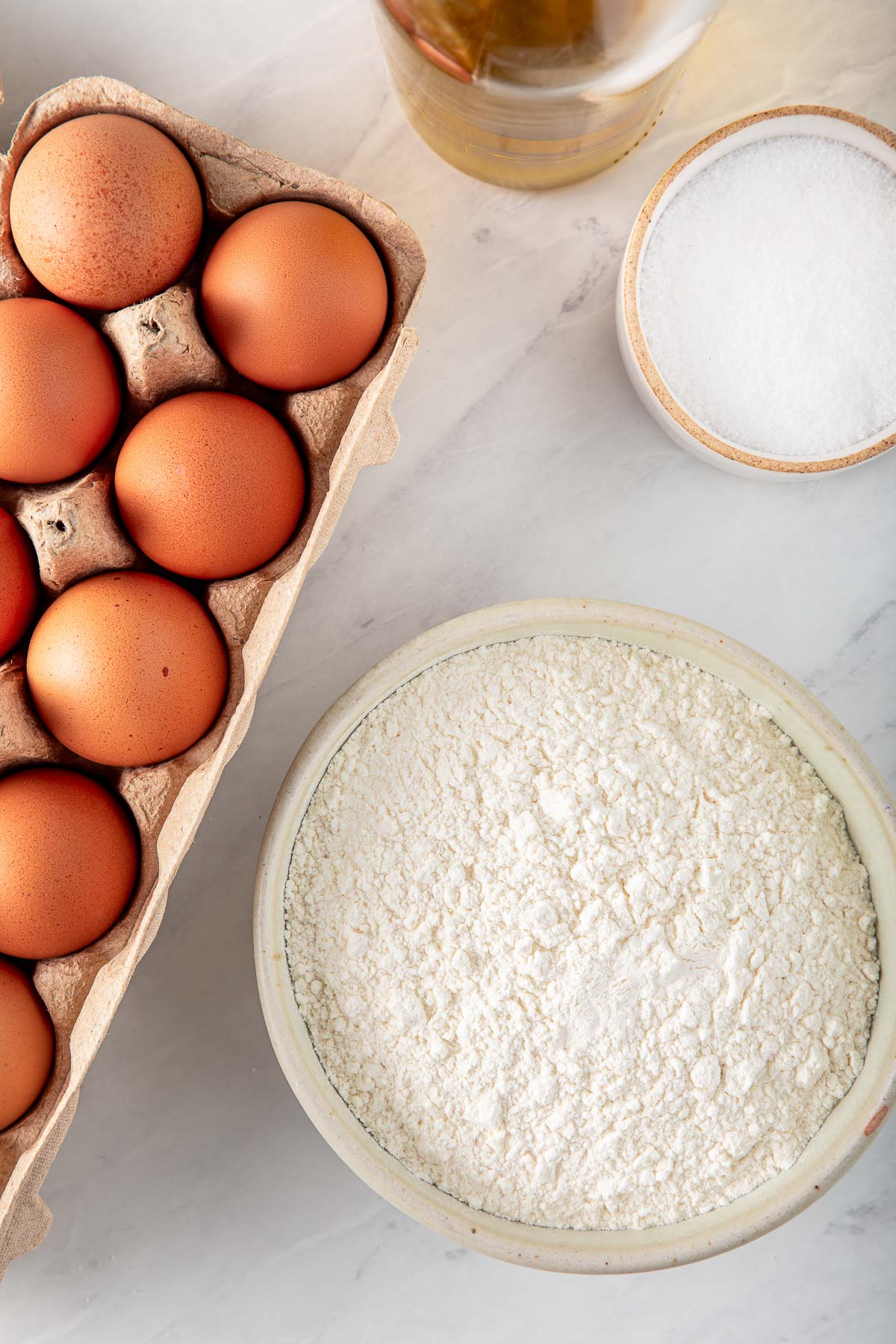 ingredients for homemade pasta - carton of eggs, bowl of flour, bowl of salt.