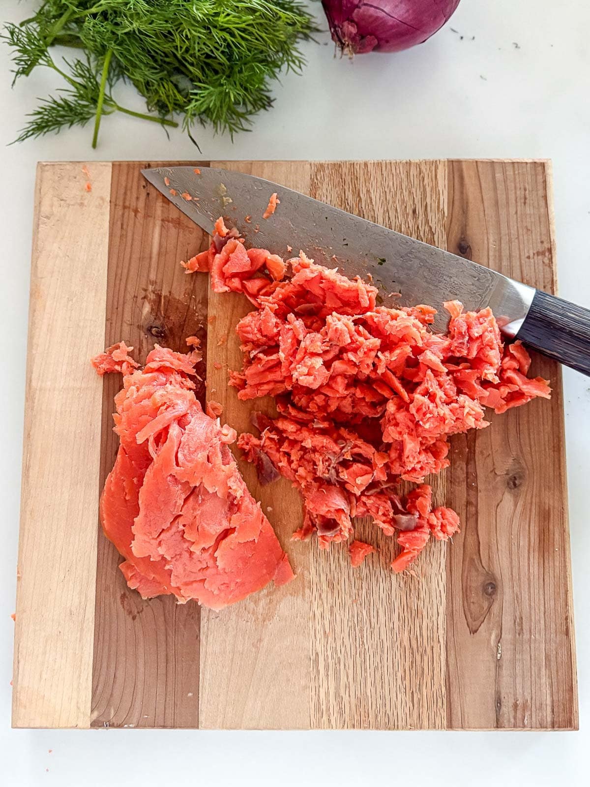 sharp knife dicing smoked salmon on wood board. 