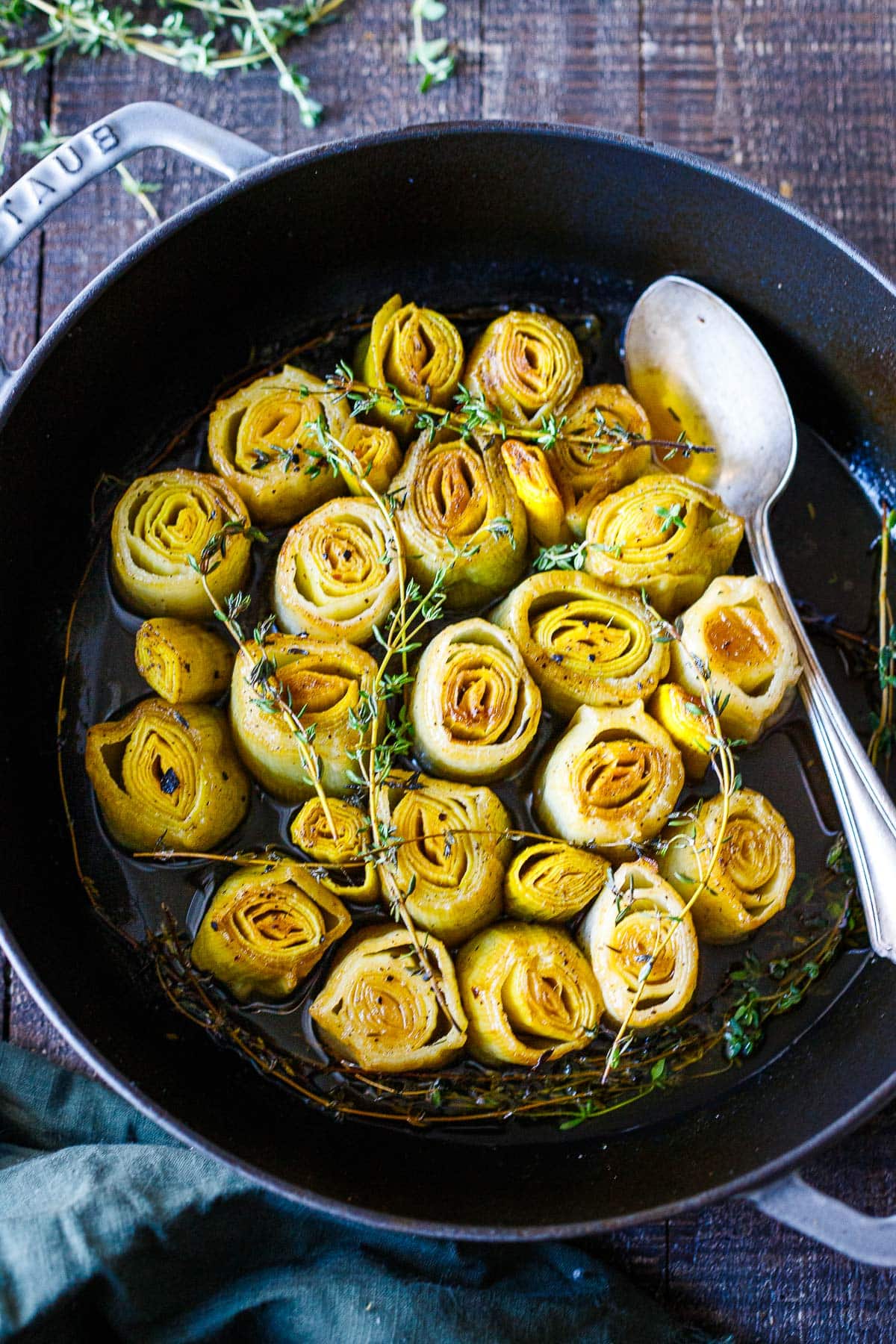 cast iron pan with braised leeks topped with thyme sprigs with spoon. 