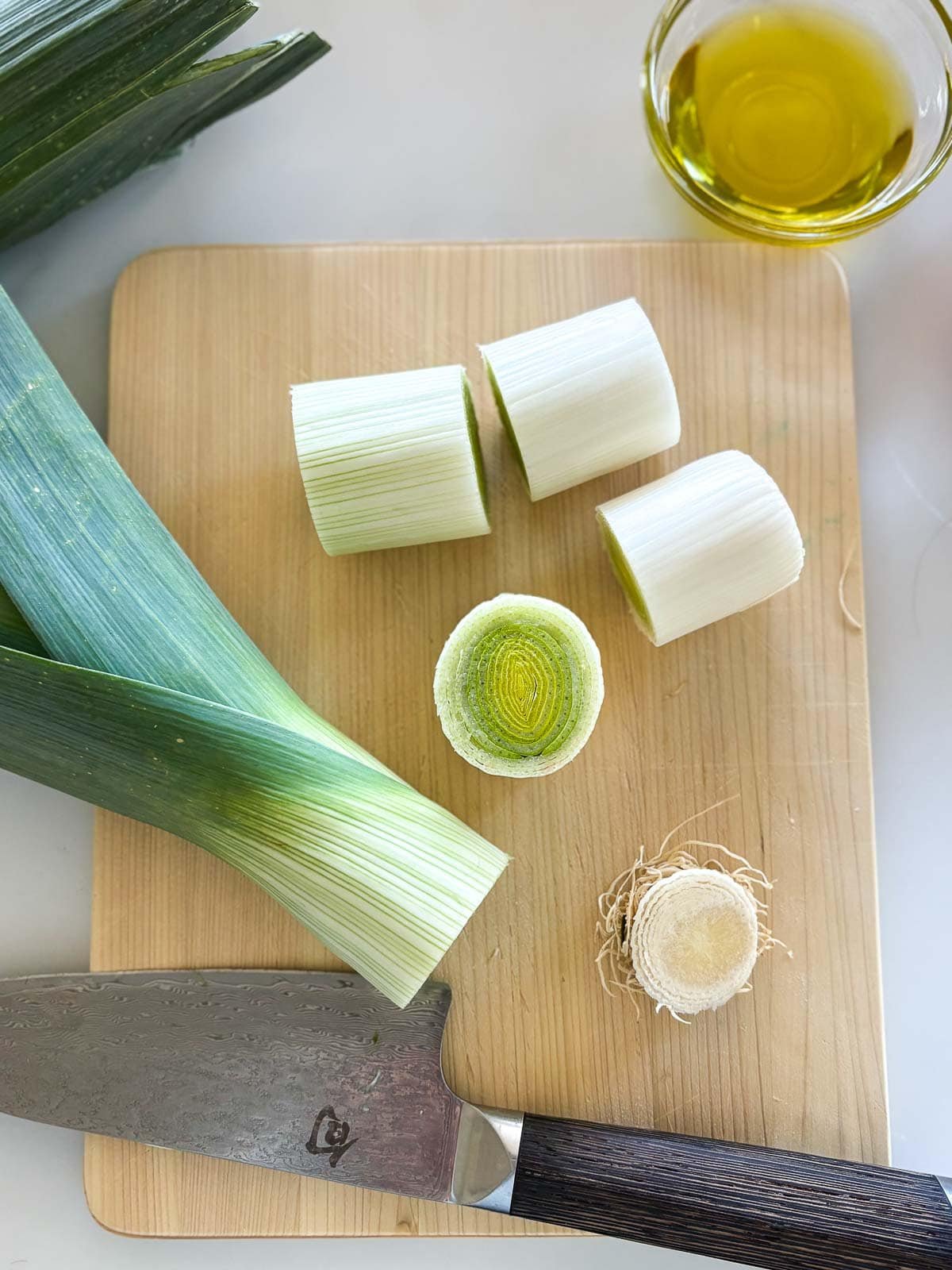 thick slices of leek on wood cutting board with sharp knife.