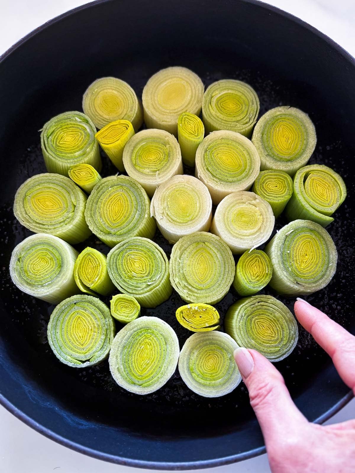 hand arranging leek slices in cast iron pan. 