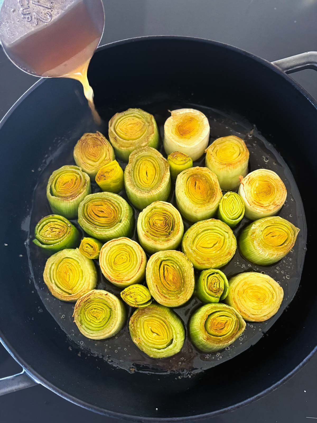 pouring broth into braiser with leeks. 
