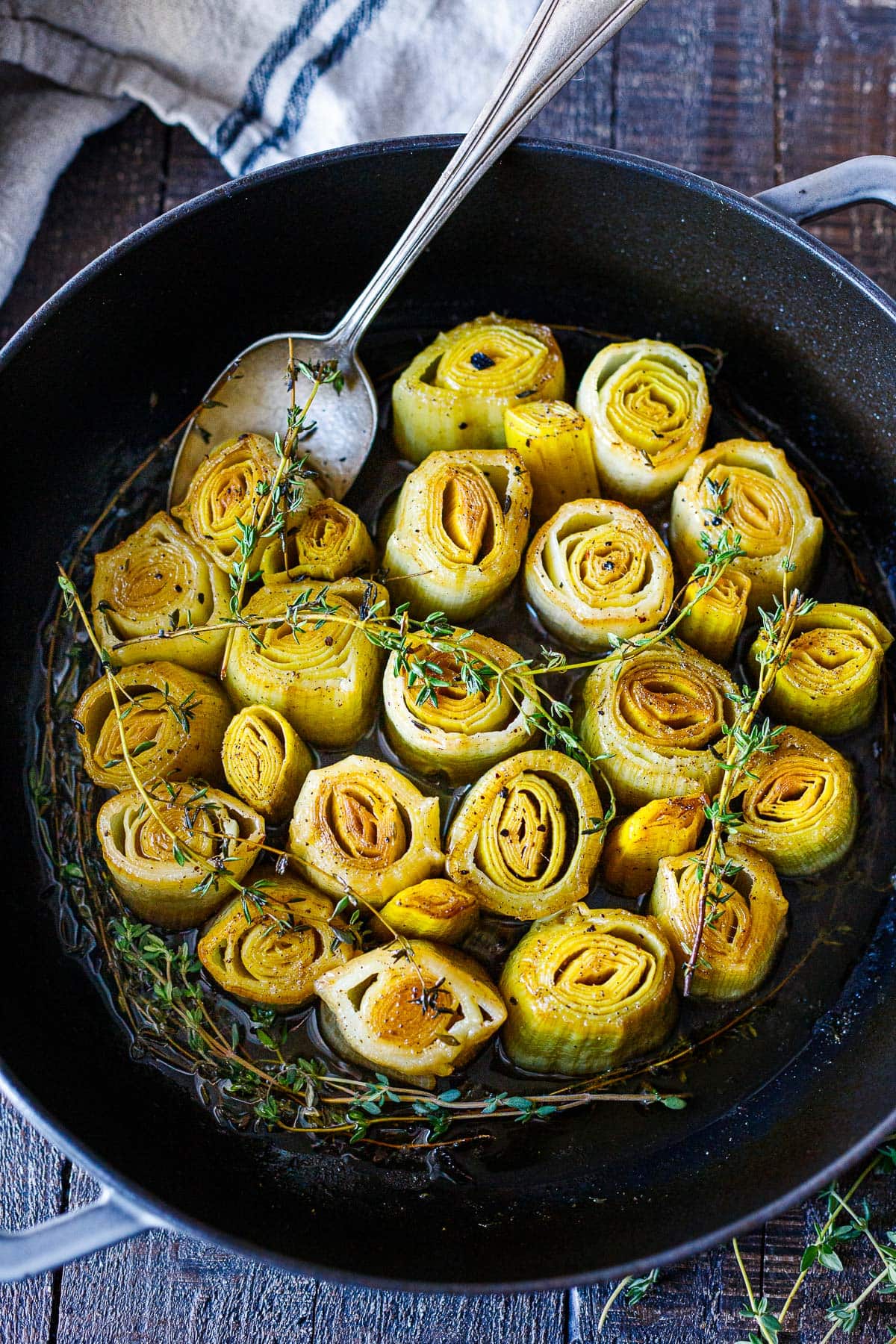 braised leeks in pan in braising liquid topped with thyme sprigs. 