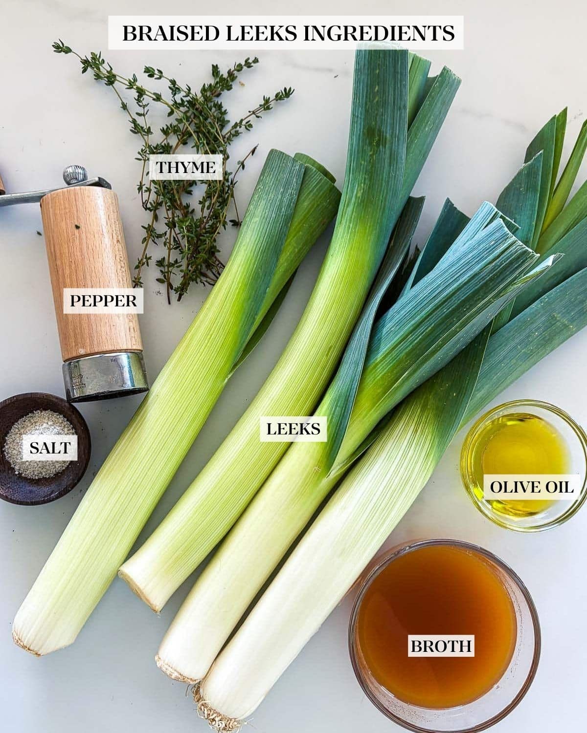 ingredients for braised leeks laid out - thyme sprigs, pepper shaker, flaky salt, four leeks, bowl of oil, bowl of broth.