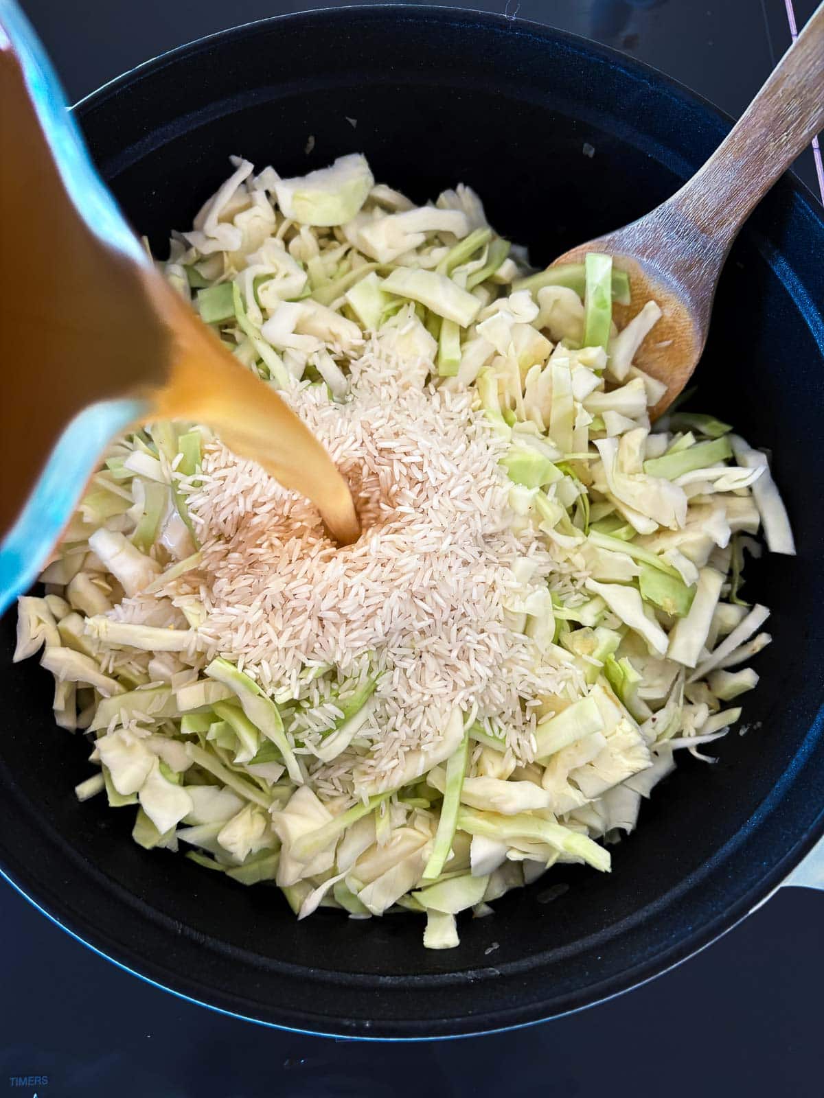 pouring broth into pot with green cabbage and rice. 