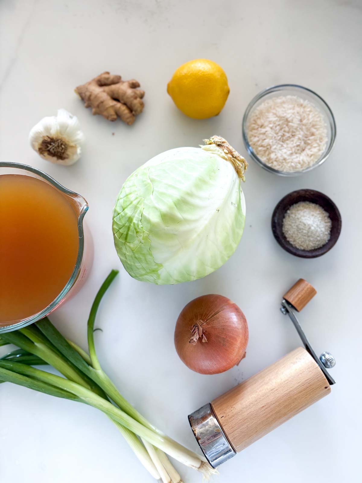 ingredients for cabbage rice soup - lemon, ginger, garlic, rice, cabbage, salt, pepper shaker, onion, broth, green onions. 