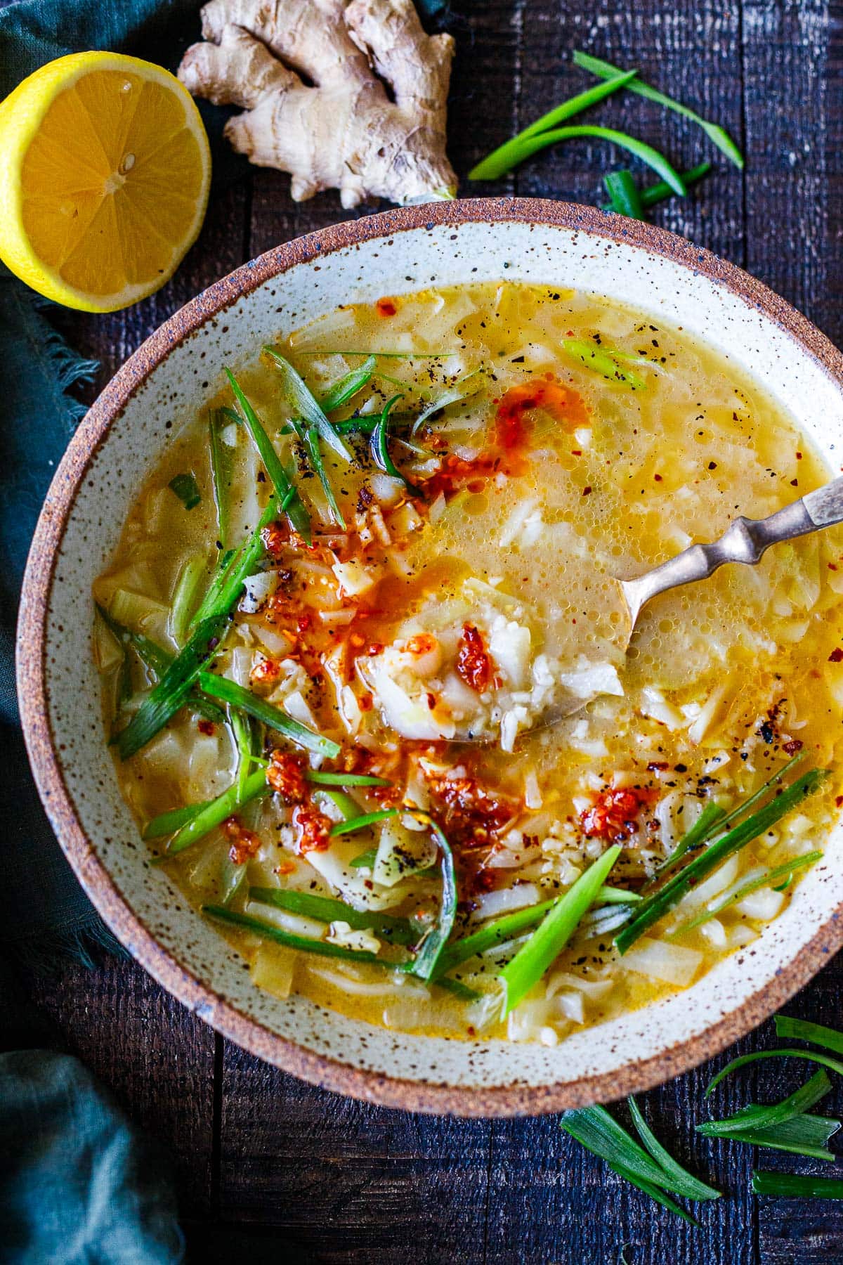 bowl of cabbage rice soup with spoon, garnished with green onions, chili flakes, and chili crisp. 