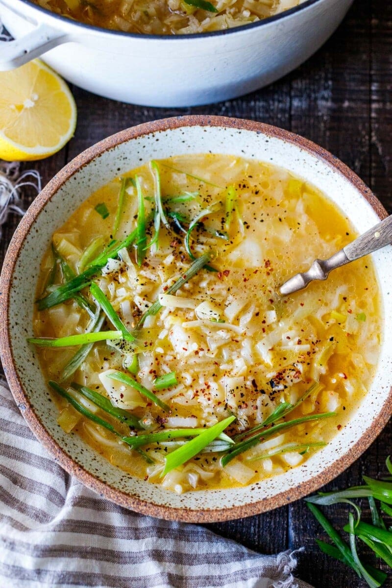 bowl of cabbage rice soup topped with green onions and chili flakes with spoon in bowl.