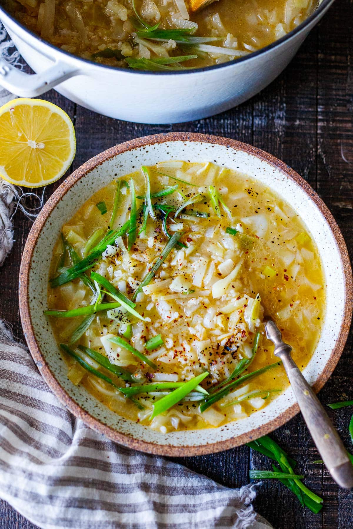 bowl of cabbage rice soup with spoon, garnished with green onions and chili flakes. 