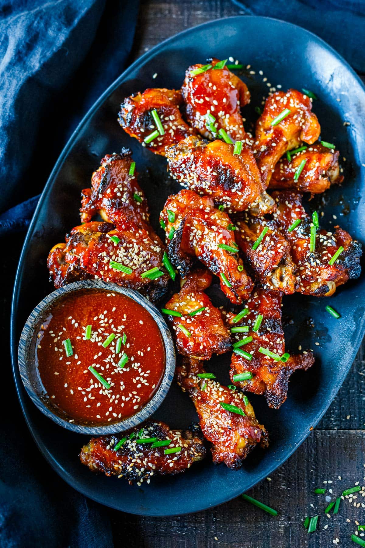 serving platter with sticky Asian chicken wings with sesame seeds and chives and bowl of dipping sauce. 