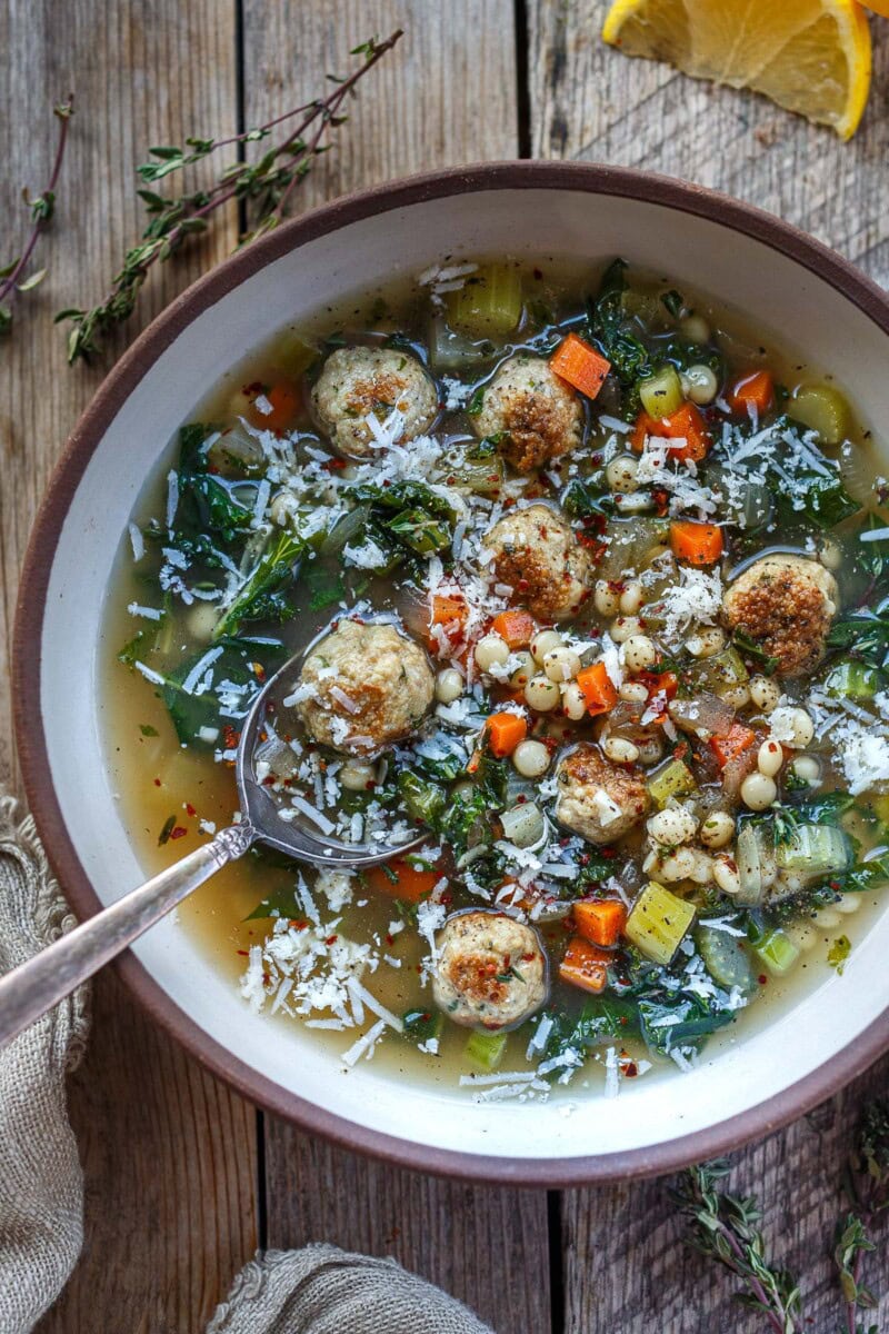 bowl of Italian wedding soup with meatballs, kale, and parmesan, with spoon. 