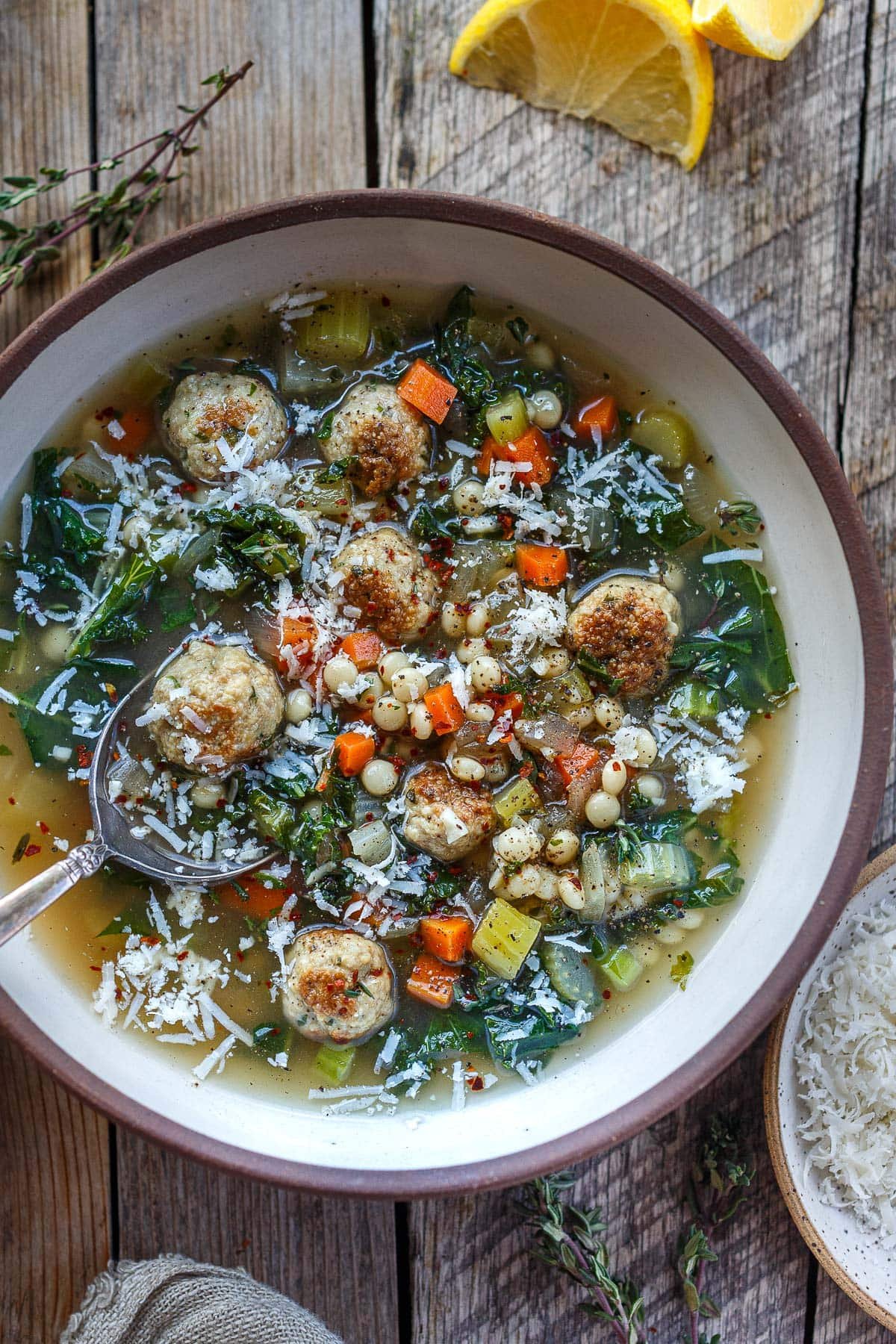 bowl of Italian wedding soup with meatballs, pearl couscous, veggies, kale, and parmesan with spoon. 