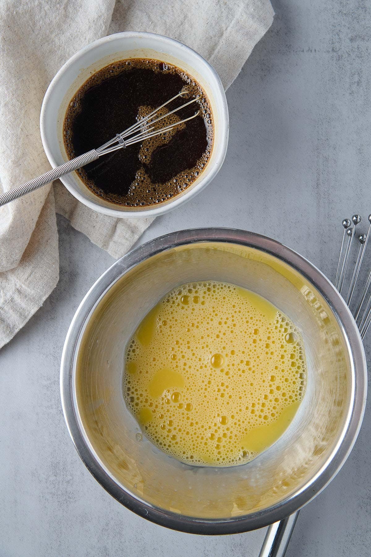 small whisk in a bowl of sauce with bowl of whisked eggs. 