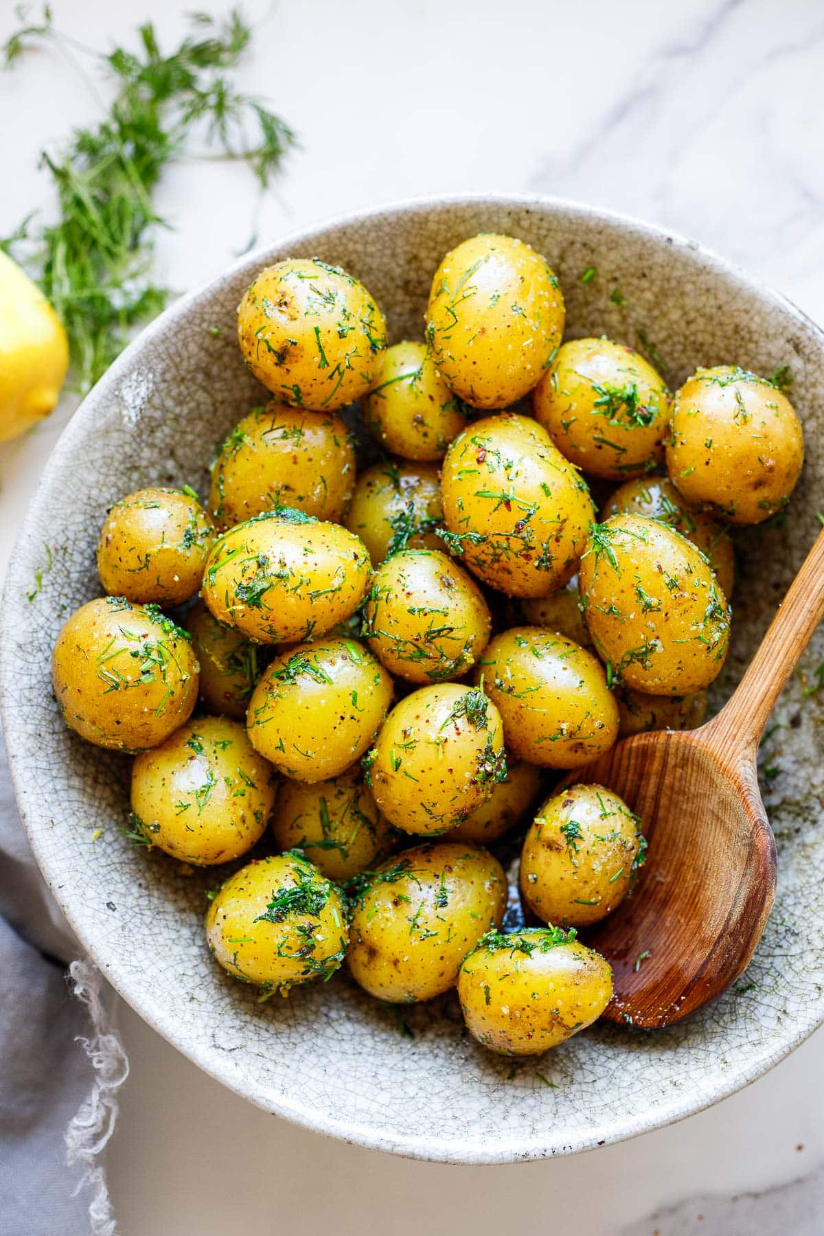 bowl of simple boiled potatoes tossed in fresh dill with wooden spoon.
