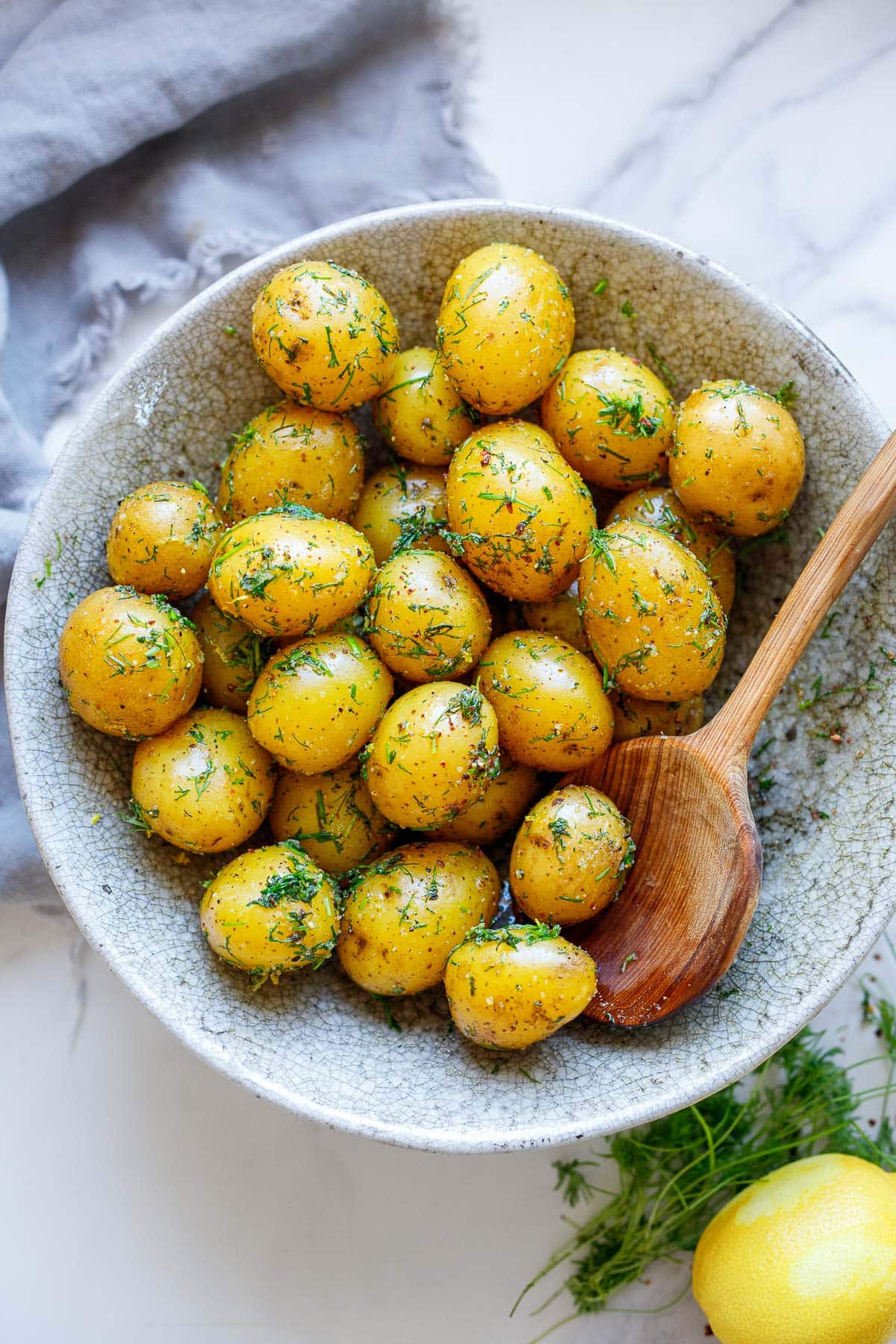bowl of boiled potatoes with fresh dill with wood serving spoon.