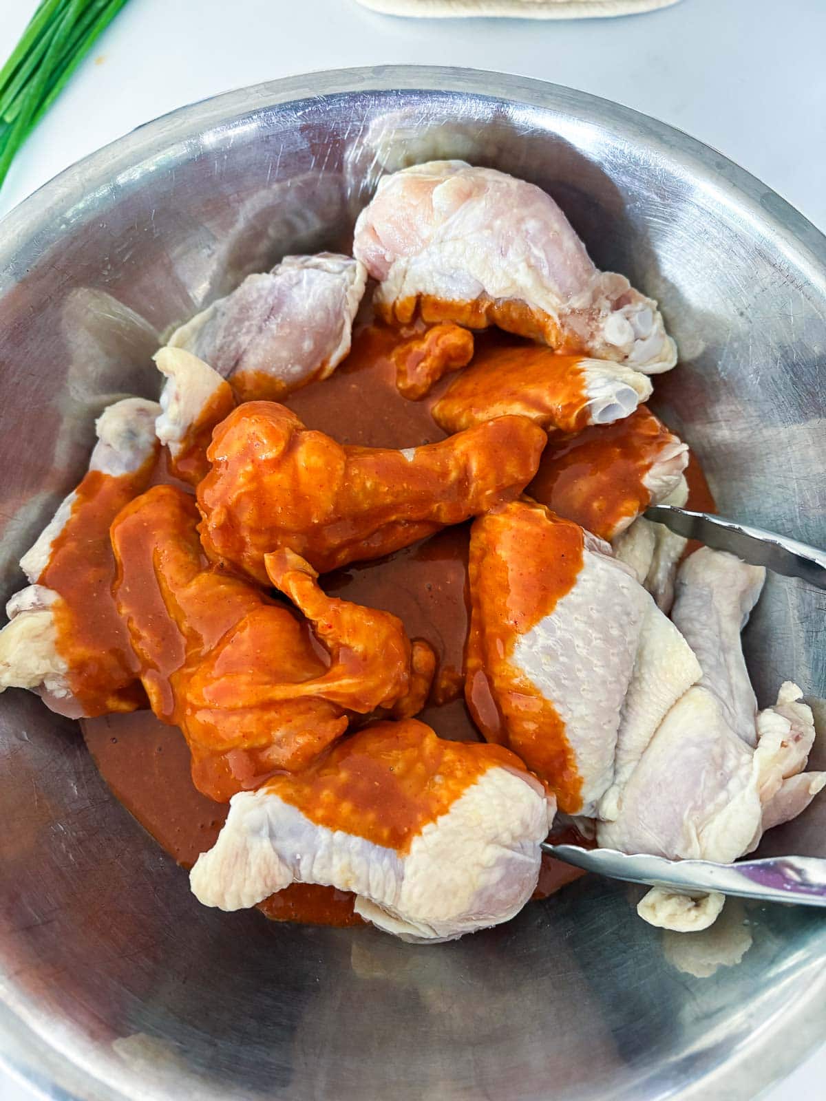 mixing bowl with tongs tossing chicken wings in marinade. 