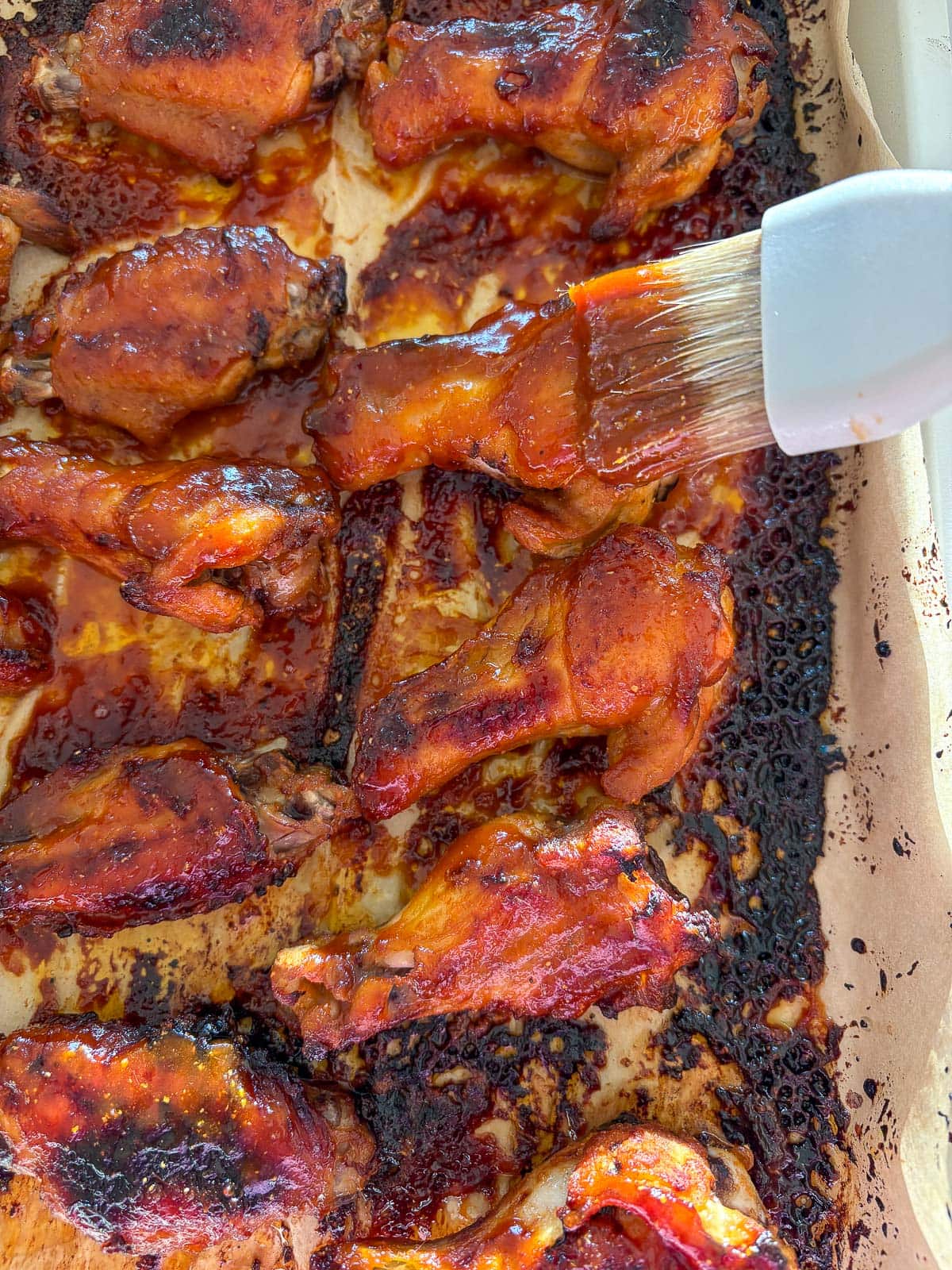 kitchen brush basting marinade on baked sticky Asian chicken wings. 