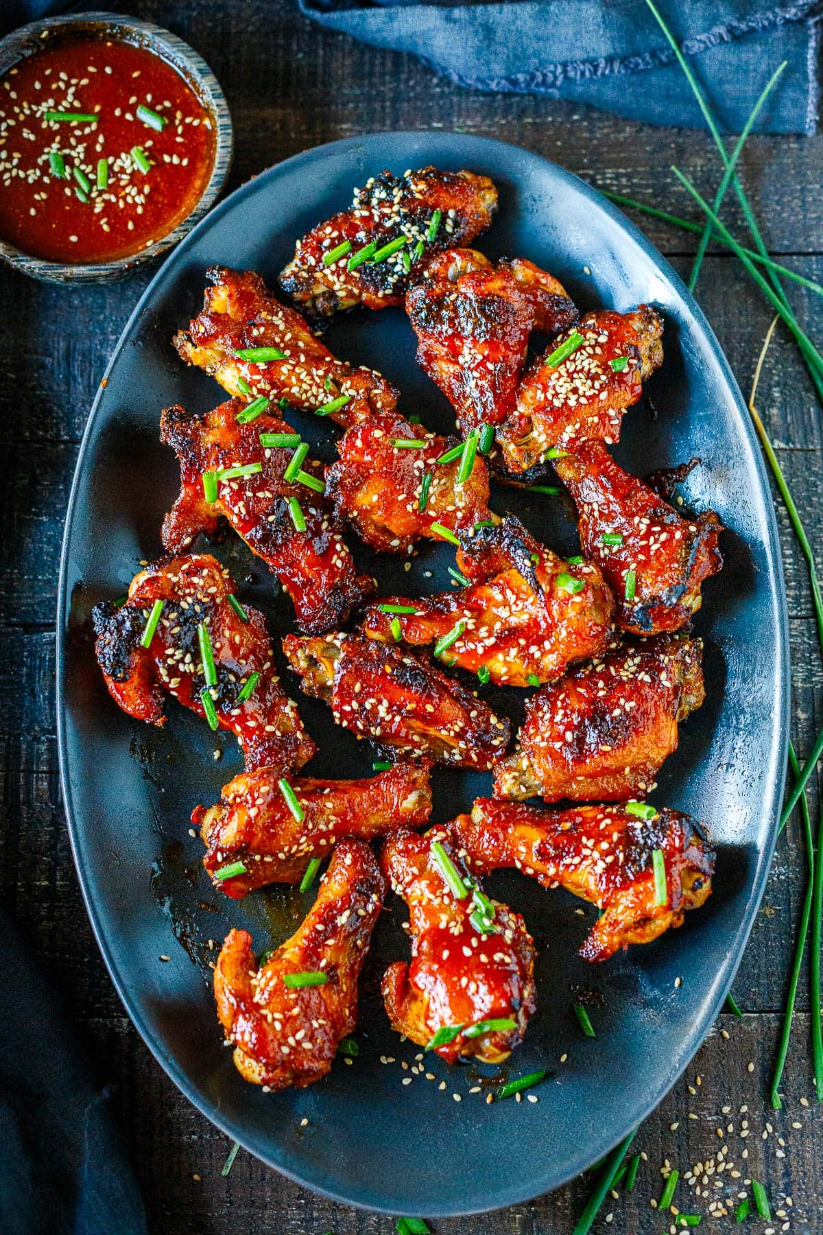 oval serving plate with sticky Asian chicken wings garnished with chives and sesame seeds. 