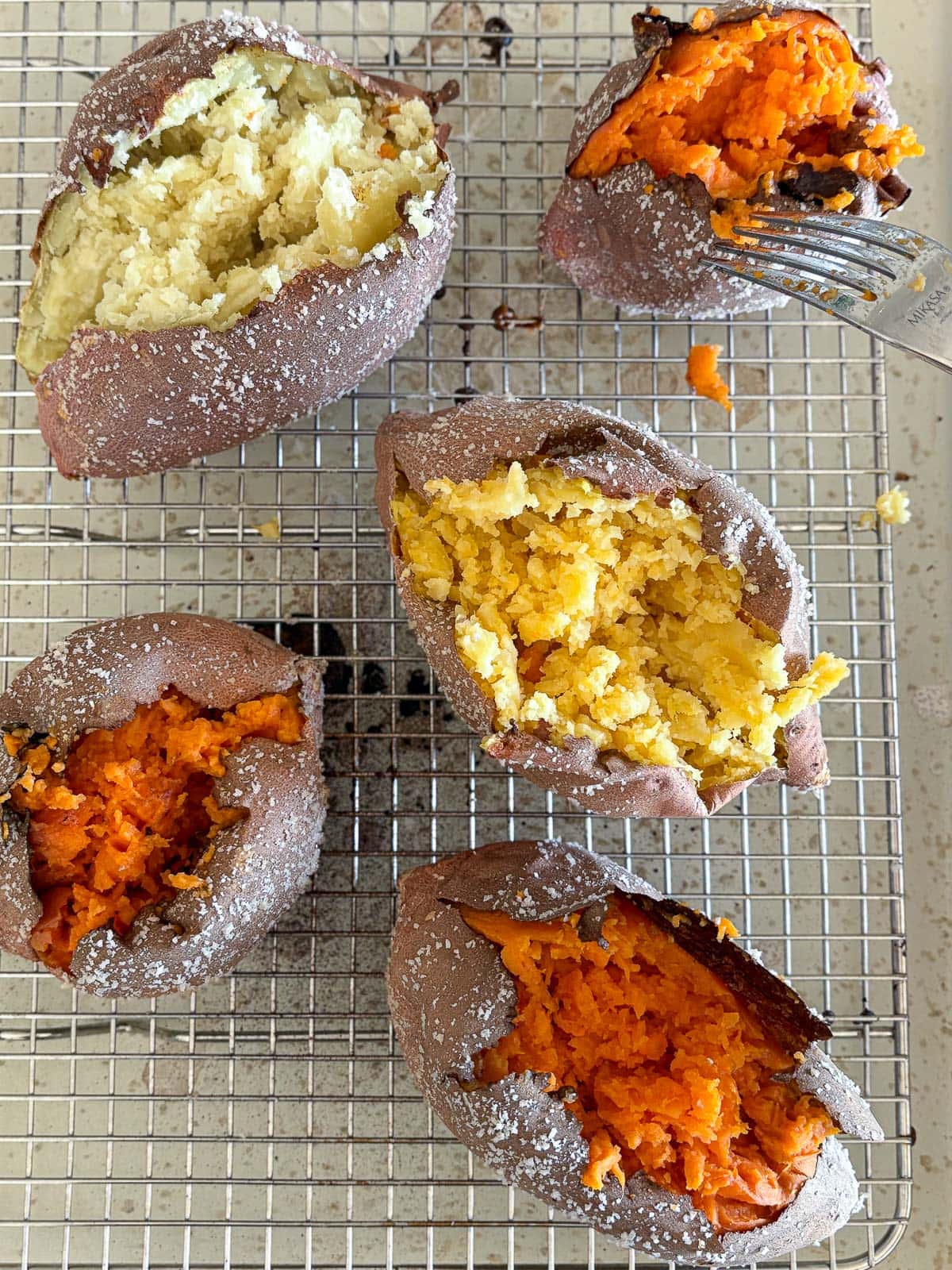 baked sweet potatoes, both regular yams and Japanese sweet potatoes, on wire rack with fork fluffing insides. 