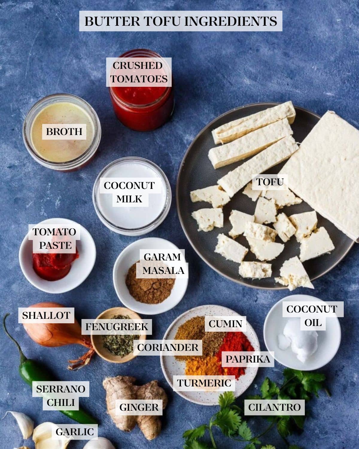 ingredients for butter tofu laid out - crushed tomatoes in jar, bowls of broth, coconut milk, tomato paste, spices, and fenugreek leaves, plate of tofu as a block, sliced, and torn, shallot, ginger, serrano pepper, garlic cloves, ginger, and cilantro.