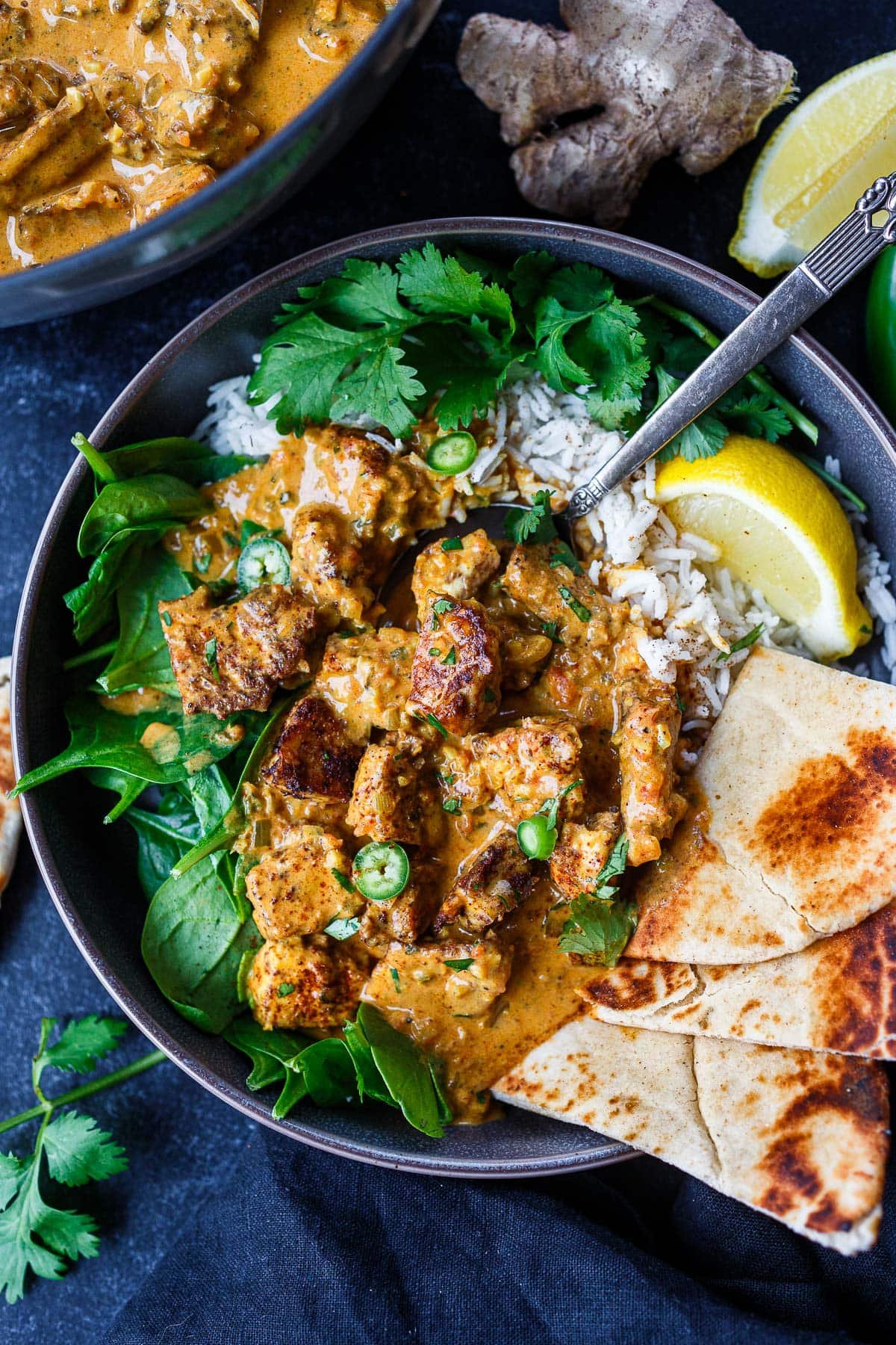 bowl of butter tofu on bed of rice and baby spinach with naan and lemon wedge.